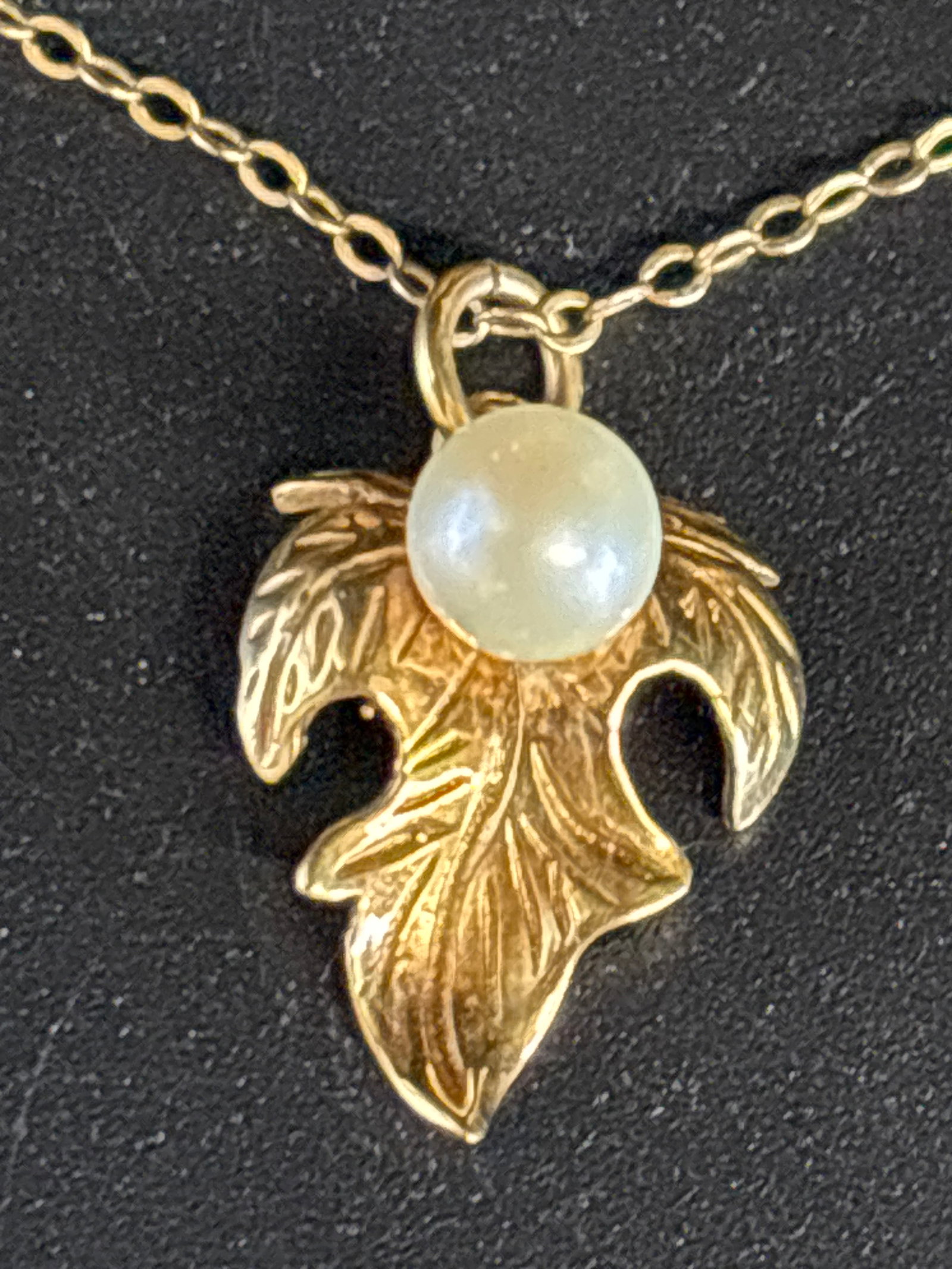 English 9 k gold pearl pendant on 9 k 20 inch chain ; 2.62 grams: vintage 9 k yellow gold leaf-shaped charm featuring a small, central pearl.Design: A detailed gold leaf or ribbon-like structure with a textured finish.Gemstone: A small white pearl sits in the