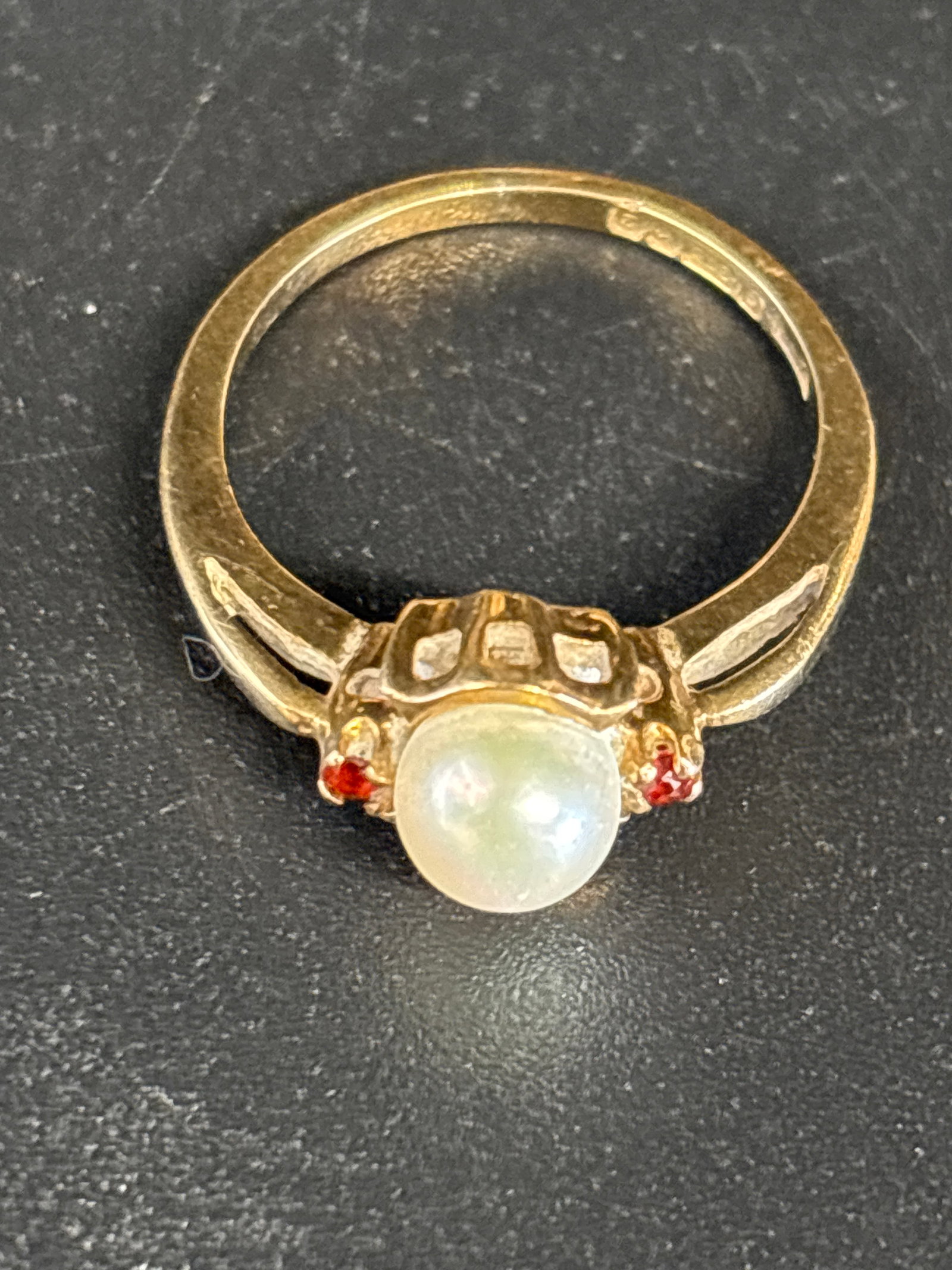 English 9 k gold pearl fashion ring ; 2.86grams: vintage 9 k yellow gold ring features a central white pearl accented by small red stones on either side.Type: Likely a fashion or vintage ring, similar antique styles exist in solid gold.Stones: The