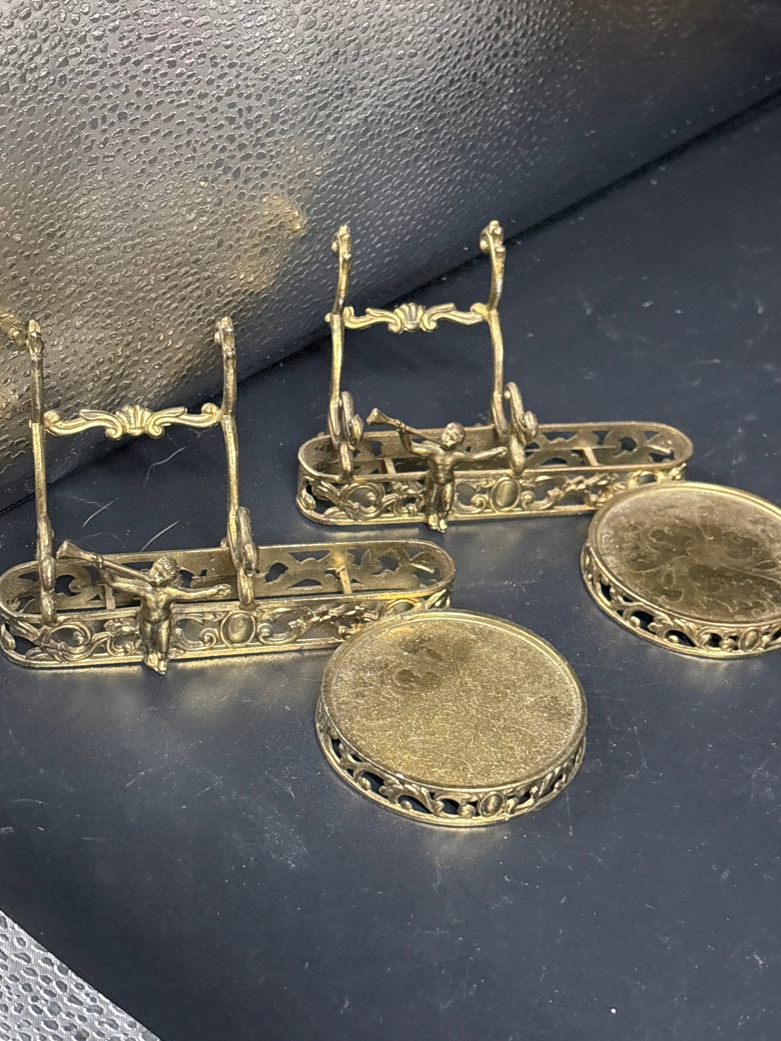 Pair vintage ornate brass display stands: vintage ornate brass display stands, often specifically used to hold teacups and saucers.They feature intricate filigree work and are commonly adorned with small cherub or angel figures.Many similar
