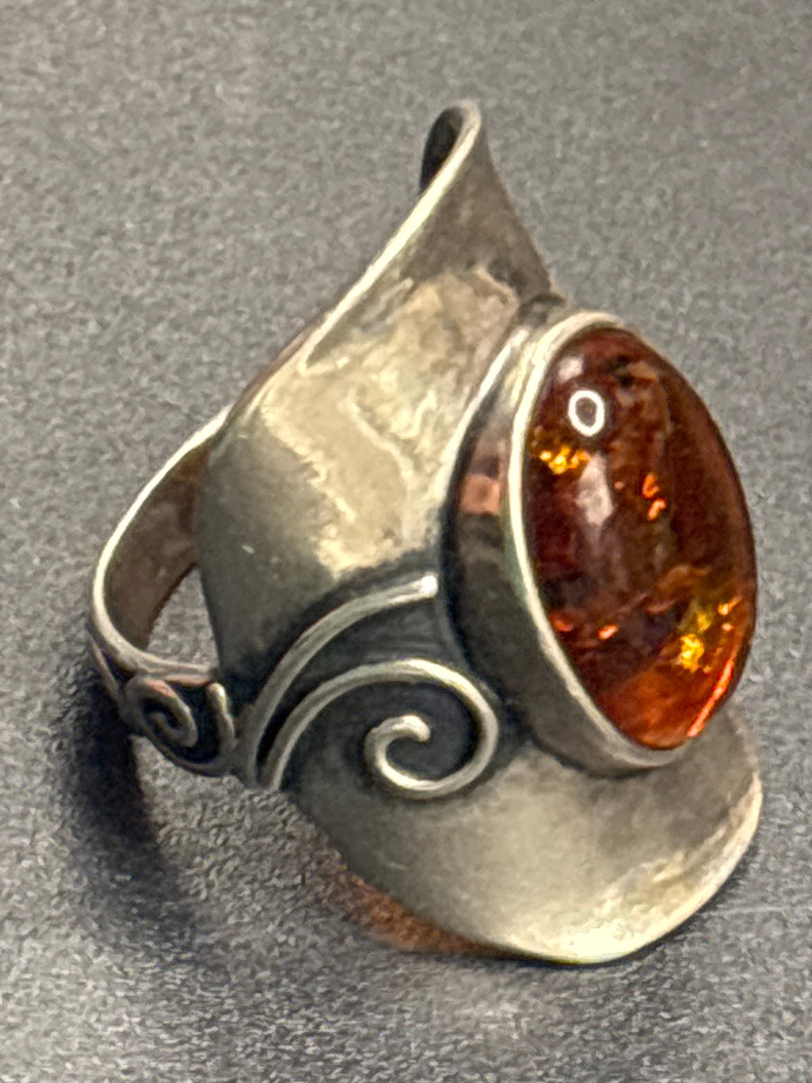 Israel vintage sterling silver large oval amber cabochon set ring: silver ring features a large oval amber cabochon set in a stylized, modern band with filigree scrollwork details.Gemstone: Natural amber with a honey-brown color.Material: 925 Sterling Silver.Design: 
