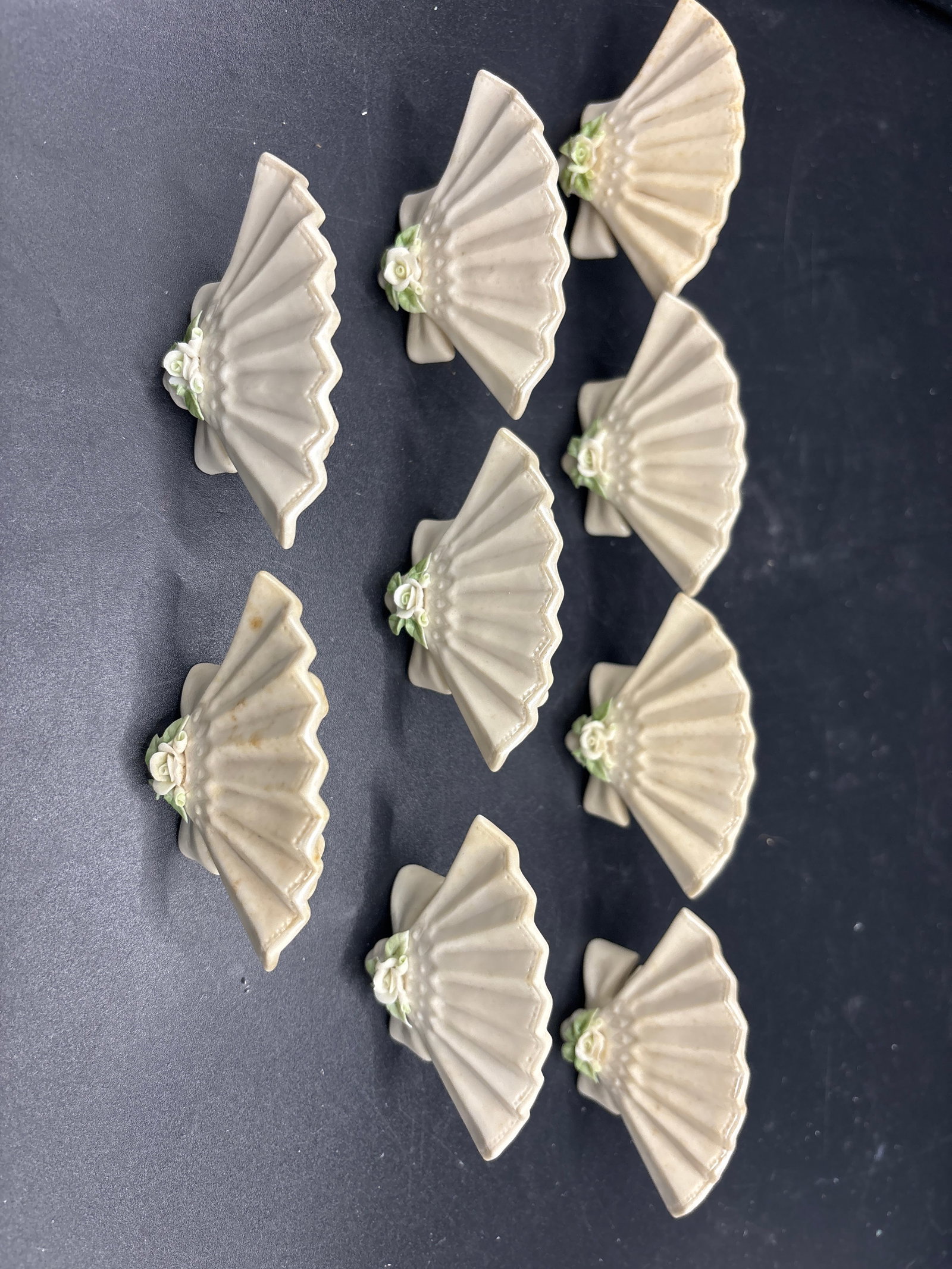 Nine Cybis porcelain fan-shaped place card holders: Cybis porcelain fan-shaped place card holders.Design Background & DetailsOrigin: These miniature tableware pieces were crafted by the renowned Cybis Porcelain Studio in Trenton, New Jersey. They were 