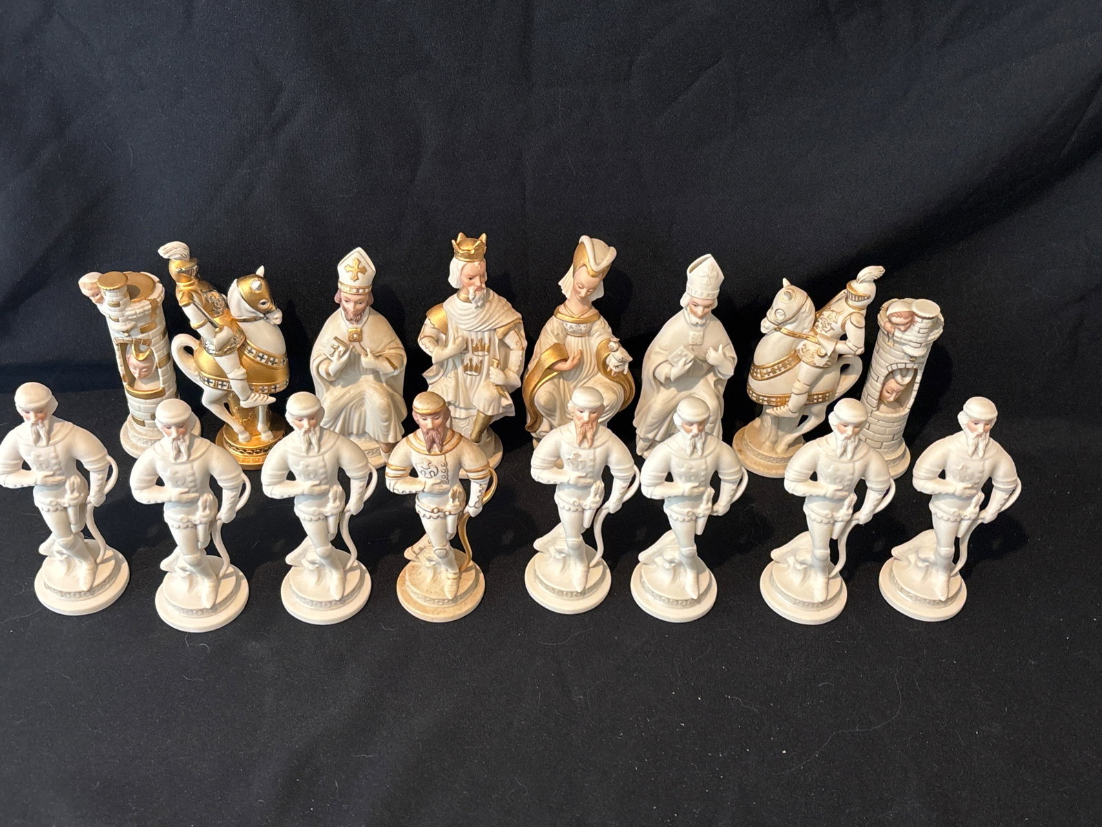 Sixteen piece similar Cybis white and gold porcelain chess figures: Sixteen piece similar Cybis white and gold porcelain figures arranged in rows, including pawns holding bows, bishops, a king, a queen, a knight, and a rook formatted as an ornate castle tower.
