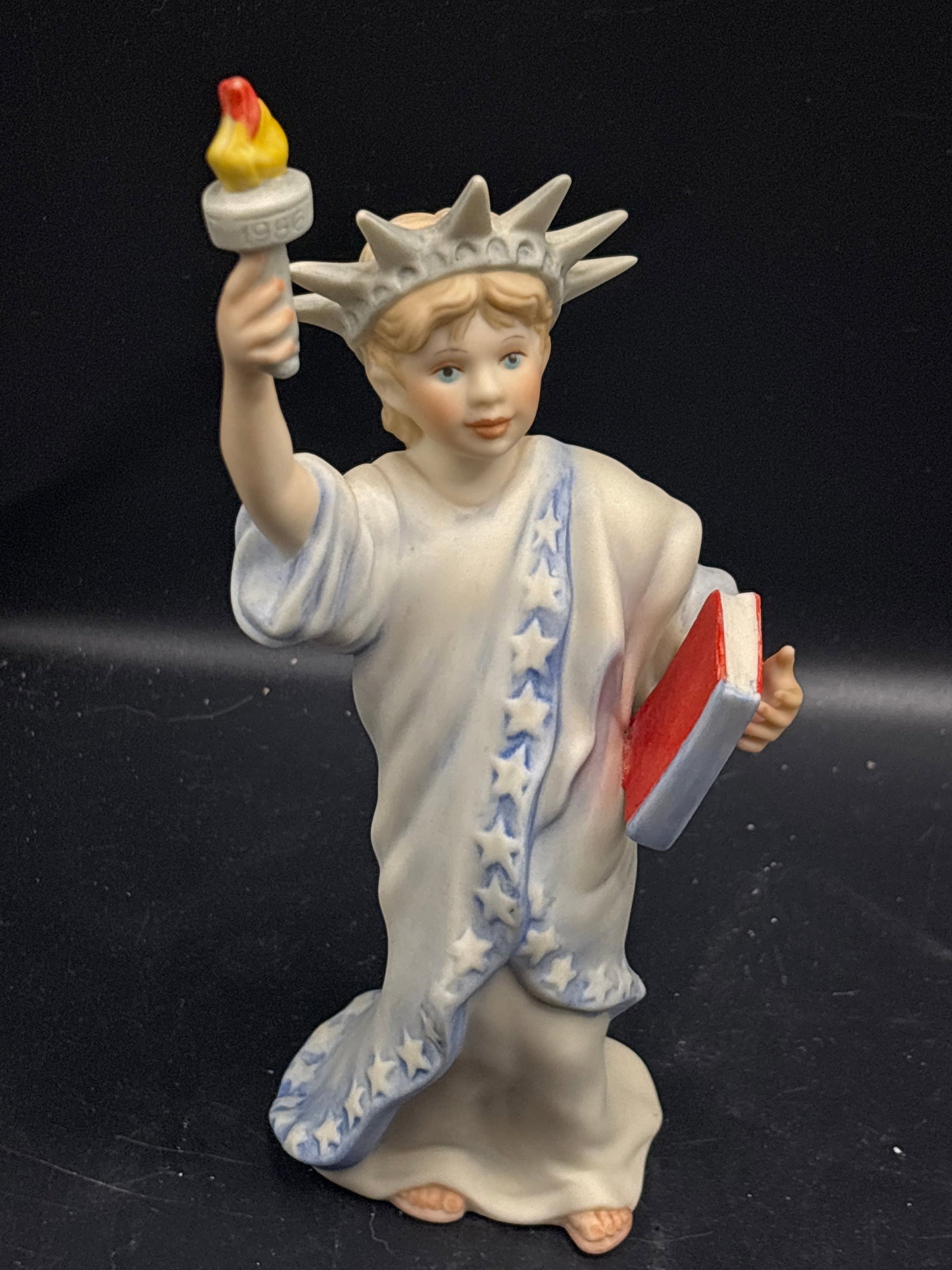 Cybis porcelain "Little Miss Liberty" figurine: "Little Miss Liberty" figurine crafted by Cybis around 1985–1986.DetailsMaker: CybisName: Little Miss LibertyFeatures: Young girl styled as the Statue of Liberty in a white gown with a blue star-pat