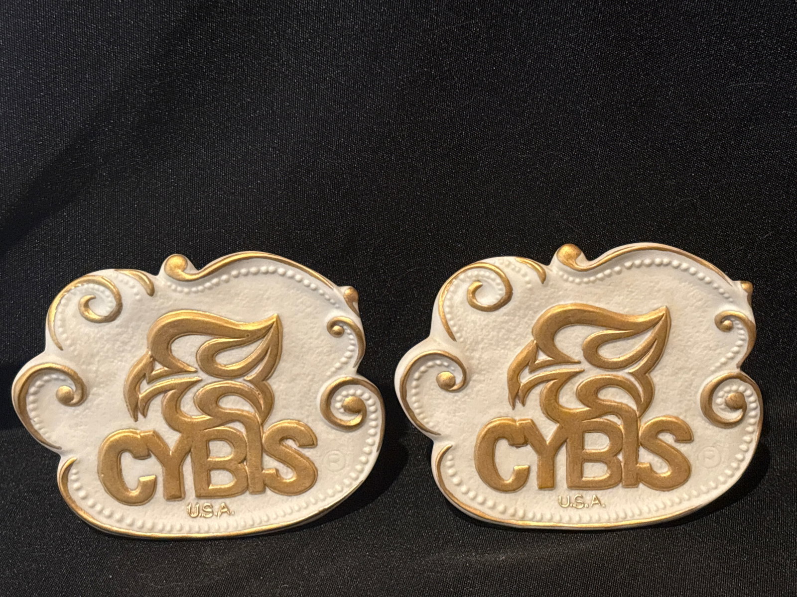 Pair Cybis porcelain freeform display signs: Pair Cybis porcelain freeform display sign featuring the brand's signature phoenix logo and gold trim.OverviewItem: Cybis dealer/display signMaterial: White bisque porcelain with gold detailingDesign:
