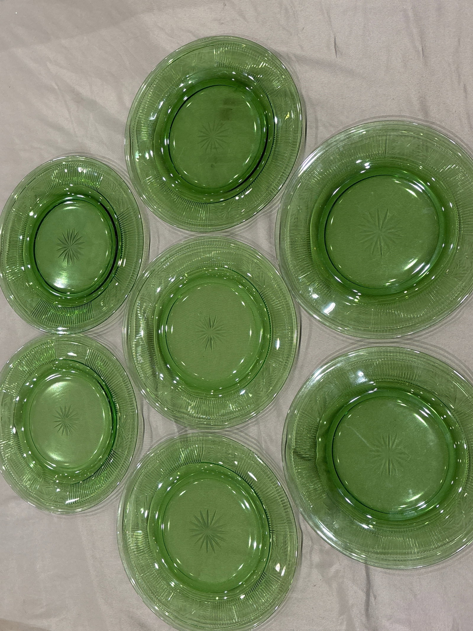 Seven Heisey Pleat and Panel pattern green glass 8 inch salad plates: Seven green glass salad plates appear to be from the Heisey Pleat and Panel pattern in the Moongleam color, produced around the 1920s.Pattern: They feature a distinctive starburst design on the center