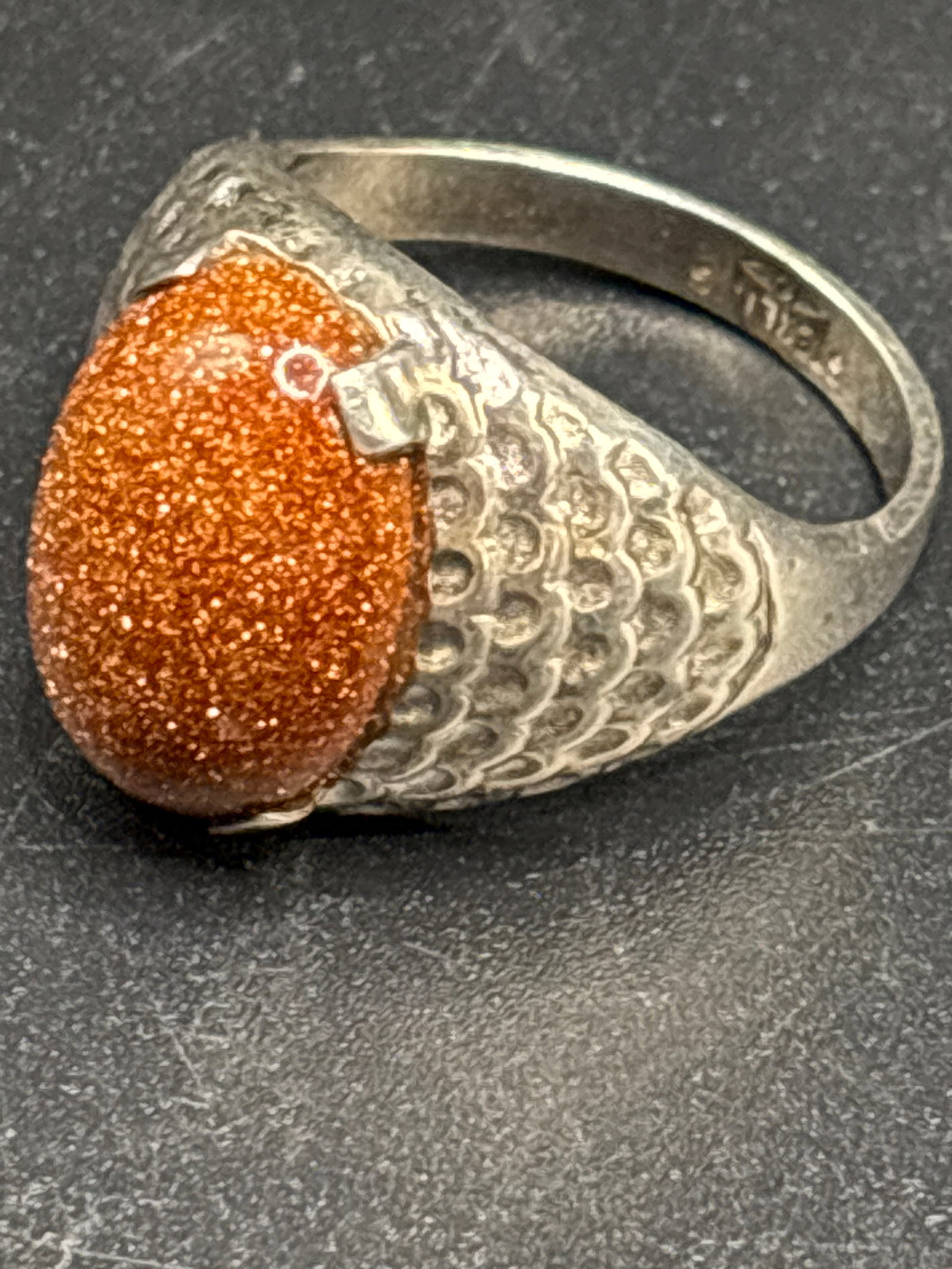 sterling silver ring features a textured band and a prominent, orange, sparkling sandstone: sterling silver ring features a textured band and a prominent, orange, sparkling sandstone gemstone.Material: The band is made of 925 sterling silver.Gemstone: The stone appears to be copper-toned san