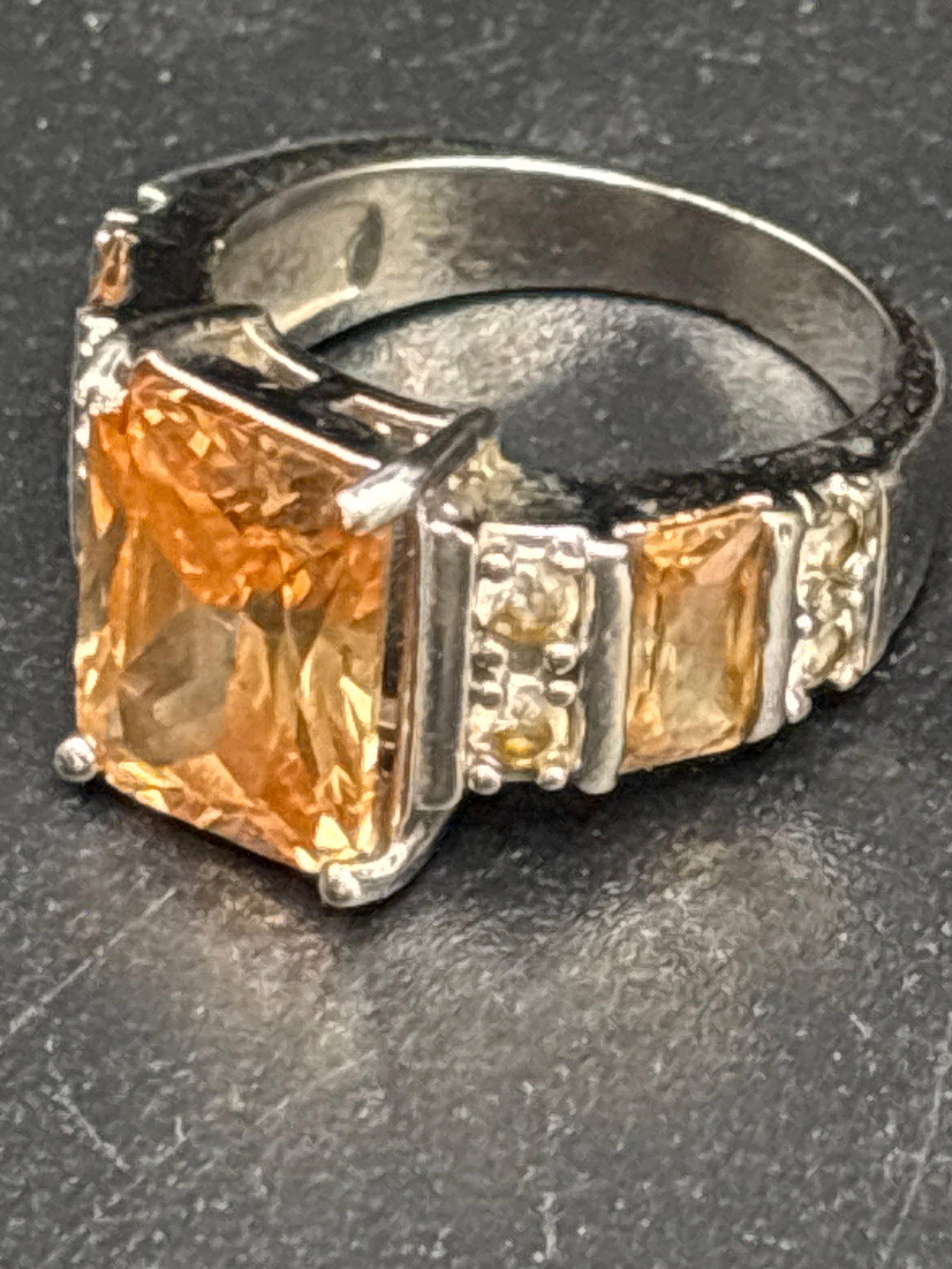 Sterling emerald cut citrine statement ring: sterling silver ring featuring a rectangular emerald-cut citrine or similar golden gemstone flanked by smaller accent stones.Material: Often listed as sterling silver (marked 925) or platinum plated.G