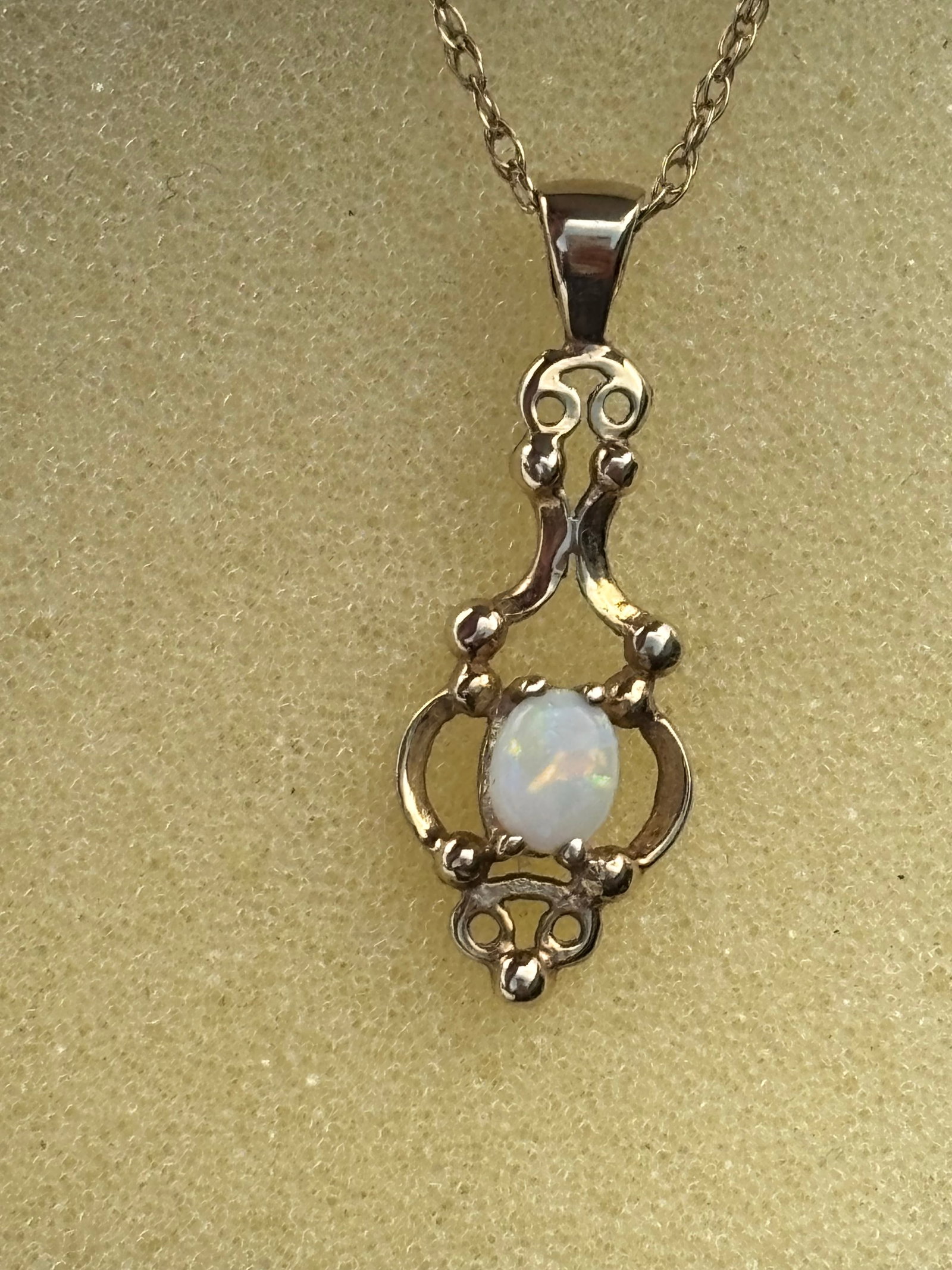 1.84 grams 9k gold lavalier pendant set with a central white opal cabochon: vintage-style 9k gold lavalier pendant set with a central white opal cabochon.Design DetailsStyle: The intricate metal framework features open scrollwork and symmetrical flourishes characteristic of E