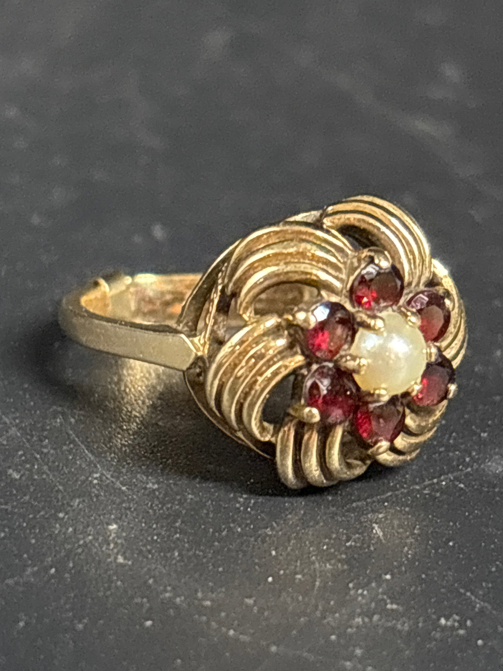 5.1 grams 9 k gold cocktail ring with cultured pearl & garnets: vintage 9k yellow gold cocktail ring featuring a central white cultured pearl surrounded by a cluster of deep red garnets (or rubies) arranged in a floral, textured swirl setting.The "9k" markup indic