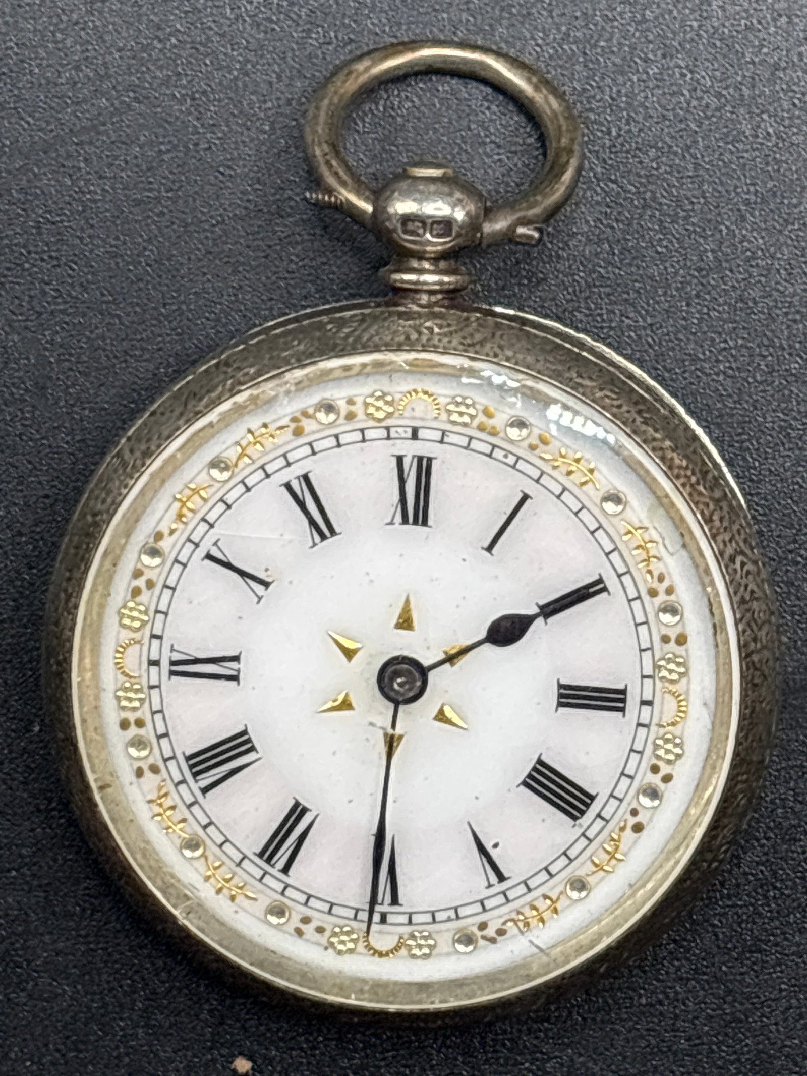 antique European open-face pocket watch: antique European open-face pocket watch, likely Swiss, featuring .935 silver casing.The watch has a white enamel dial with Roman numeral markers, gold accents, and an ornate floral design.These