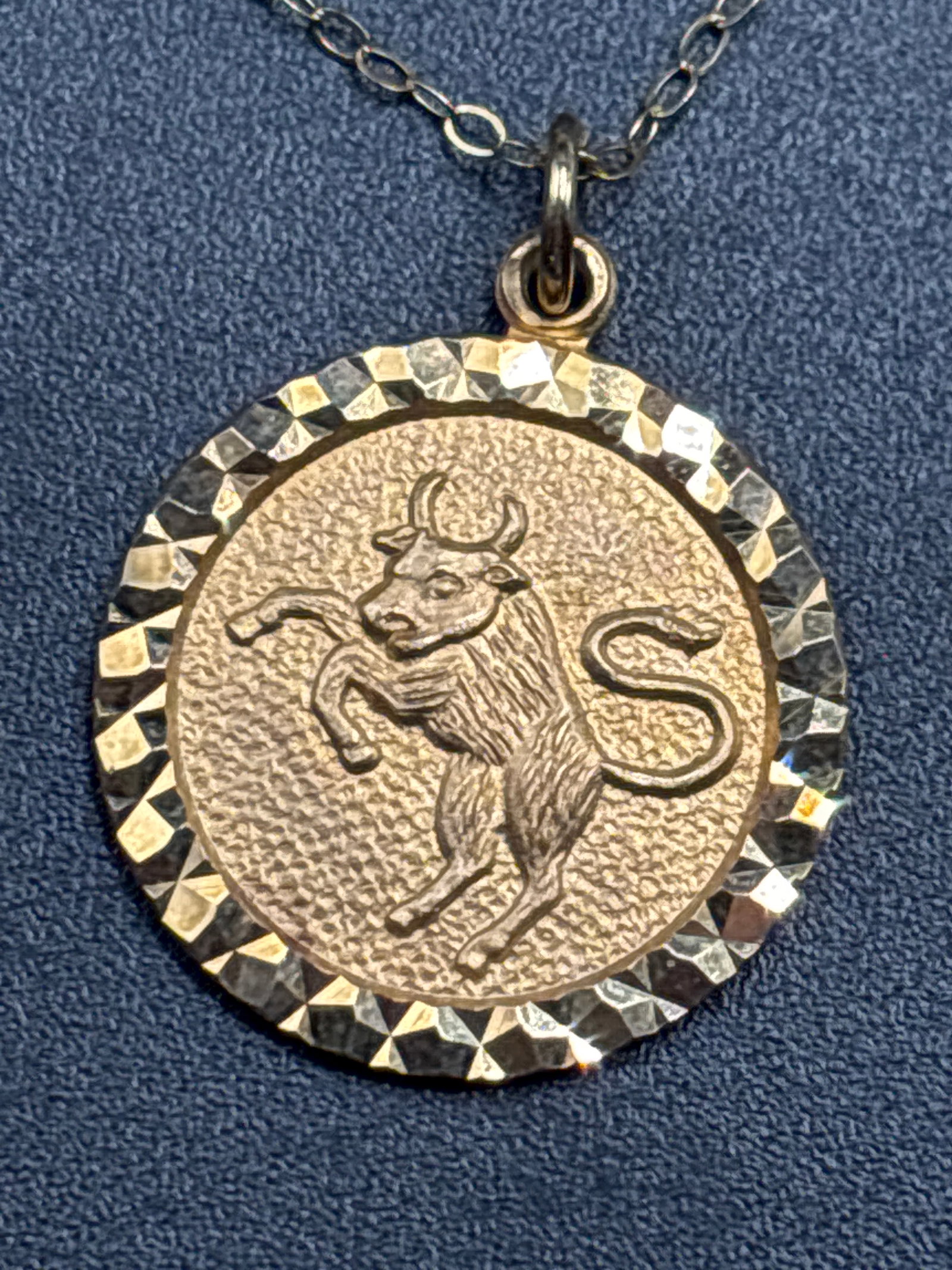 4.35 grams English 9 k yellow gold vintage-style Taurus zodiac pendant on 9 k chain: 4.35 grams English 9 k yellow gold vintage-style Taurus zodiac pendant, which features a textured central medallion depicting a rearing bull alongside an "S"-shaped tail configuration and is framed