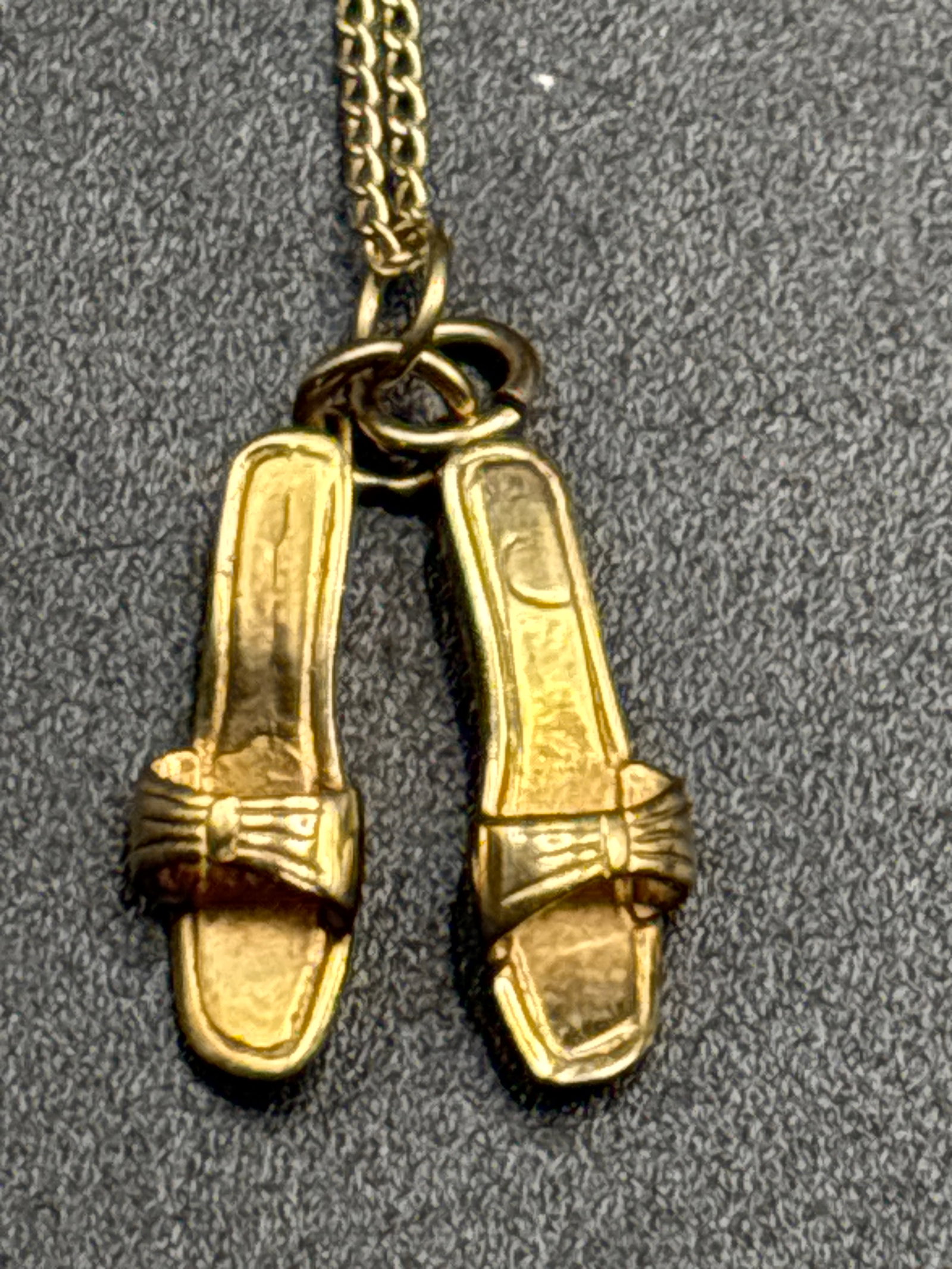 4.12 grams 14 k yellow gold twin-sandal shoe charm dangling from a fine link chain: 4.12 grams vintage 14K yellow gold twin-sandal shoe charm dangling from a fine link chain.Key Details & MarkingsMaterial Stamp: The flat circular tab attaching the shoes to the chain is stamped with a