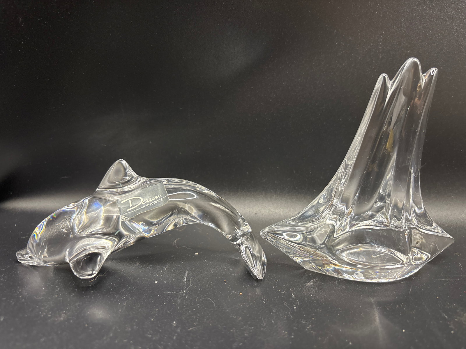 Two vintage Daum France clear crystal glass dolphin & sailboat figurines: Two vintage Daum France clear crystal glass dolphin & sailboat figurines, typically featuring an etched signature.The piece is often described as a paperweight or a small art glass sculpture,