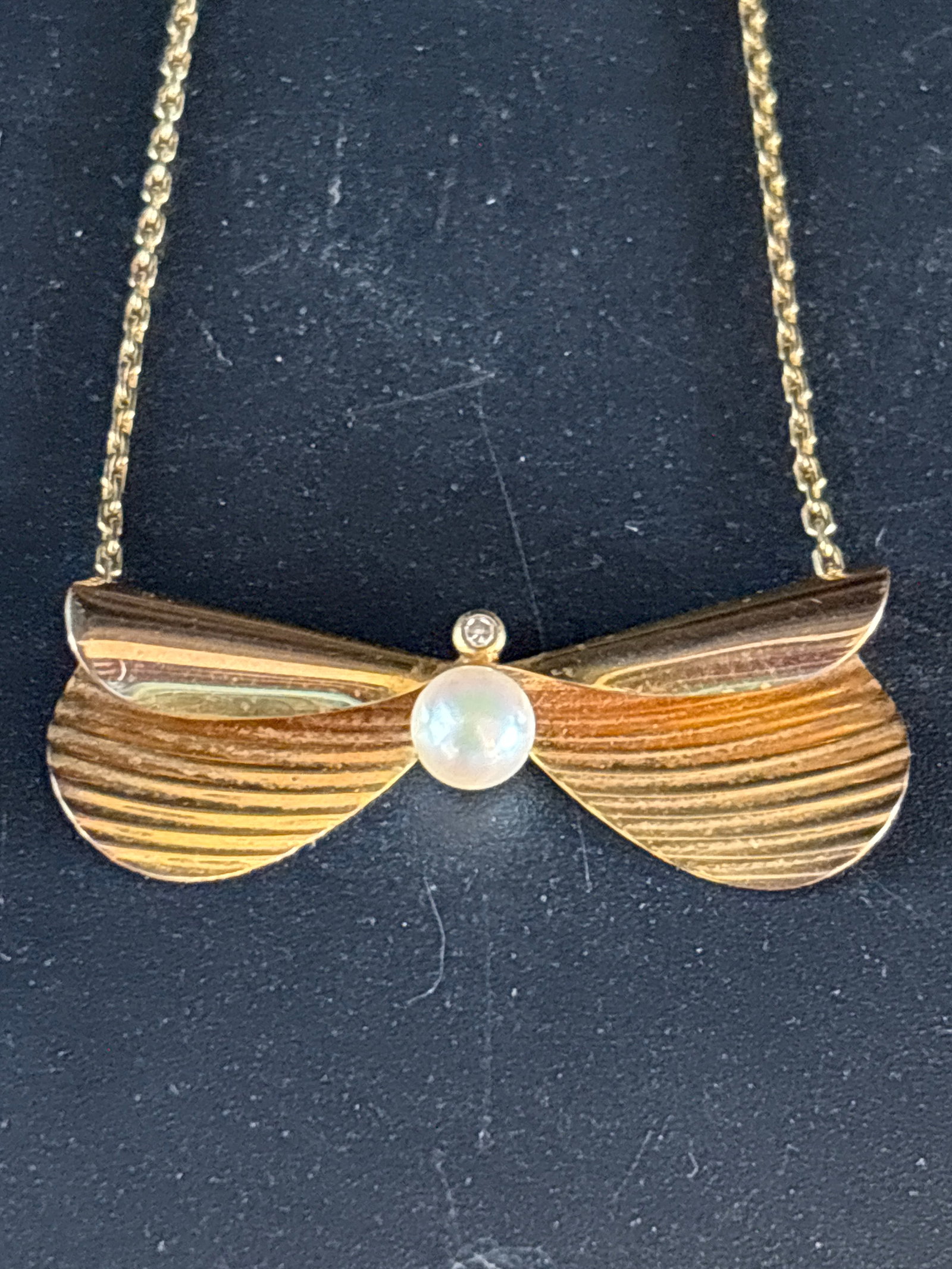 3.7 grams vintage 9-karat yellow gold bow necklace: 3.7 grams vintage 9-karat yellow gold necklace featuring an art-deco or mid-century retro style pendant.Design DetailsPendant Style: The centerpiece mimics a textured, fluted abstract bow or stylized 