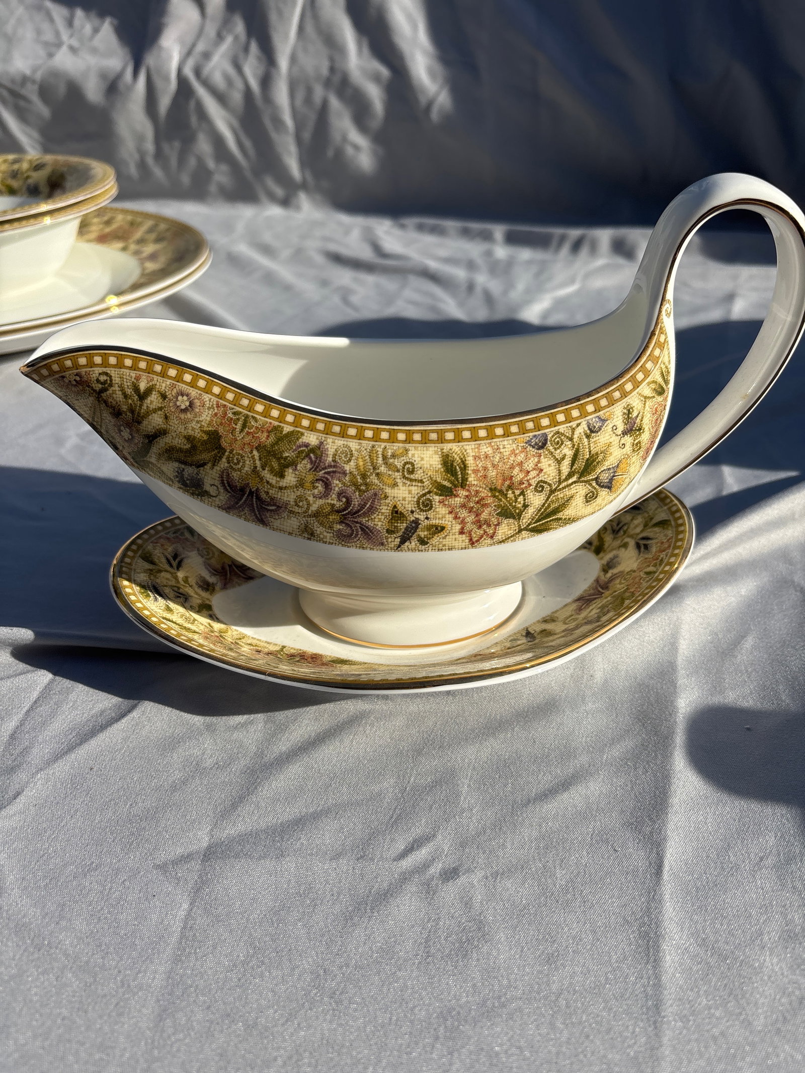Wedgwood Floral Tapestry gravy boat & underplate: Wedgwood Floral Tapestry gravy boat & underplate crafted from fine bone china in England.Pattern Details: Features a textured olive and sage green border with multicolored floral sprays, subtle bee mo
