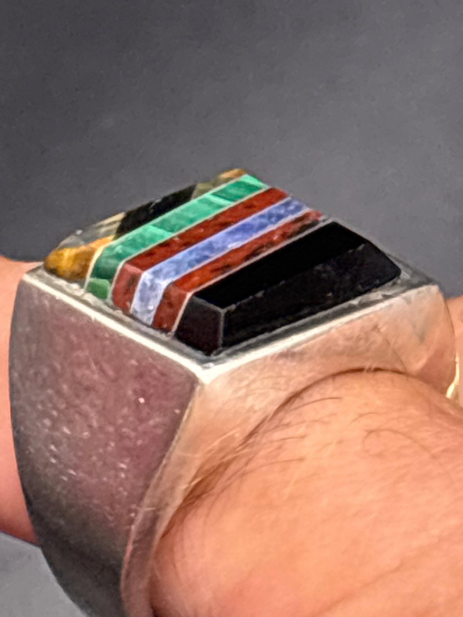 24 grams .950 Sterling southwestern-style sterling silver inlaid ring: 24 grams Sterling southwestern-style sterling silver ring features a geometric multi-stone channel inlay with alternating bands of black onyx, red coral or jasper, blue lapis, green malachite, and tig