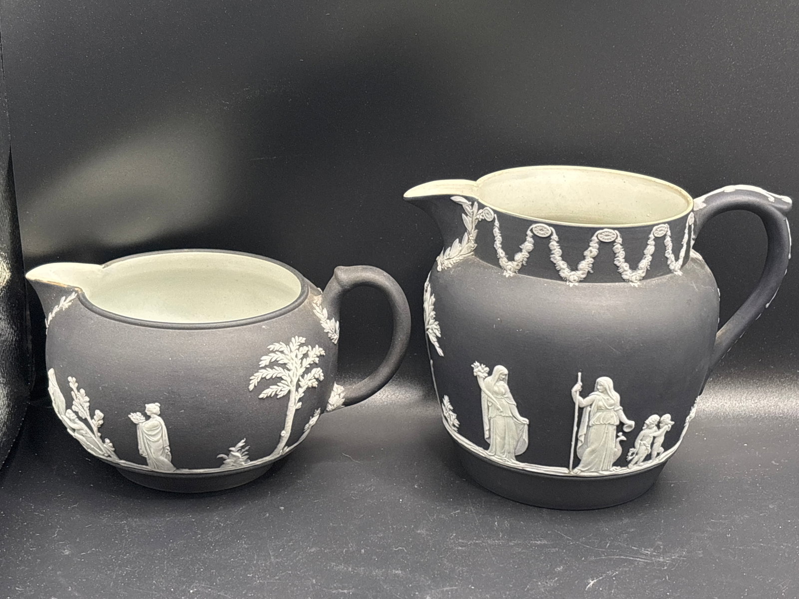 Two antique Wedgwood black jasperware milk jug/pitchers: Two antique Wedgwood black jasperware milk jug/pitchers.This specific piece is styled in a "black jasper dip" finish, which is highly sought after by collectors. It features standard matte stoneware e