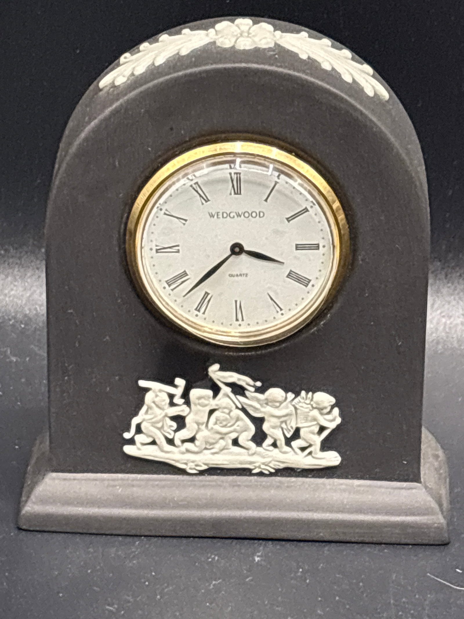 vintage Wedgwood black jasperware arched desk clock: vintage Wedgwood black jasperware arched desk clock featuring applied white neoclassical "Boys at Play" (or romping cherubs) bas-relief ornamentation and a round gold-tone quartz dial.Material & Style