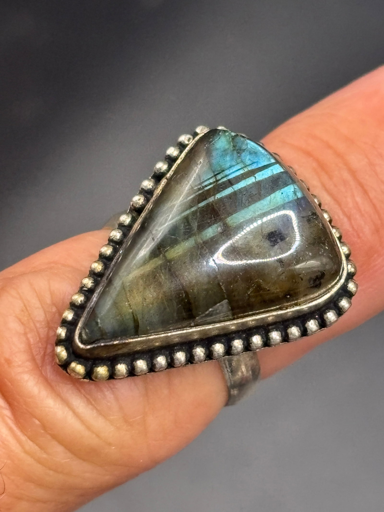 vintage sterling triangular labradorite statement ring: triangular labradorite statement ring featuring a distinctive grey-green base stone with subtle flashes of blue iridescence, known as labradorescence. The gemstone is held securely by a smooth