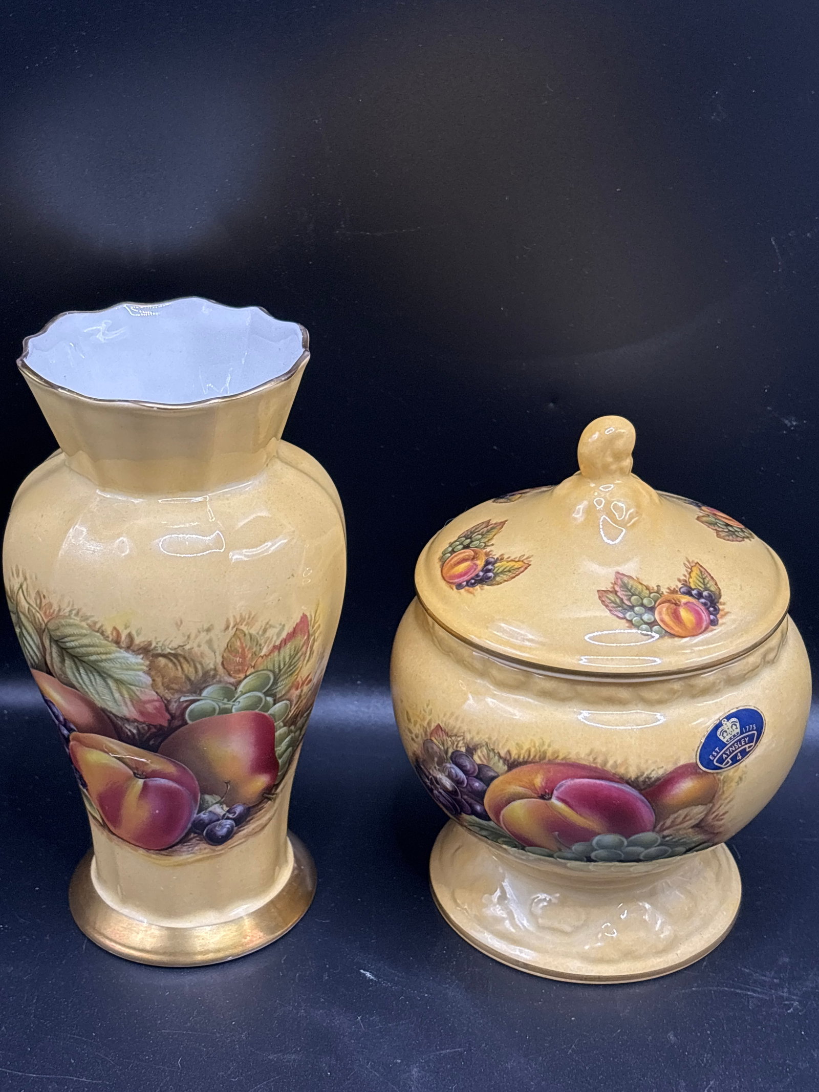 Two Aynsley "Orchard Gold" items; 6 inch vase & 4.5 inch covered jar: 6 inch vase & 4.5 inch covered jar; famous Orchard Gold collection by the historic English bone china manufacturer Aynsley Fine Bone China. About the CollectionDesign Background: The "Orchard Gold" pa