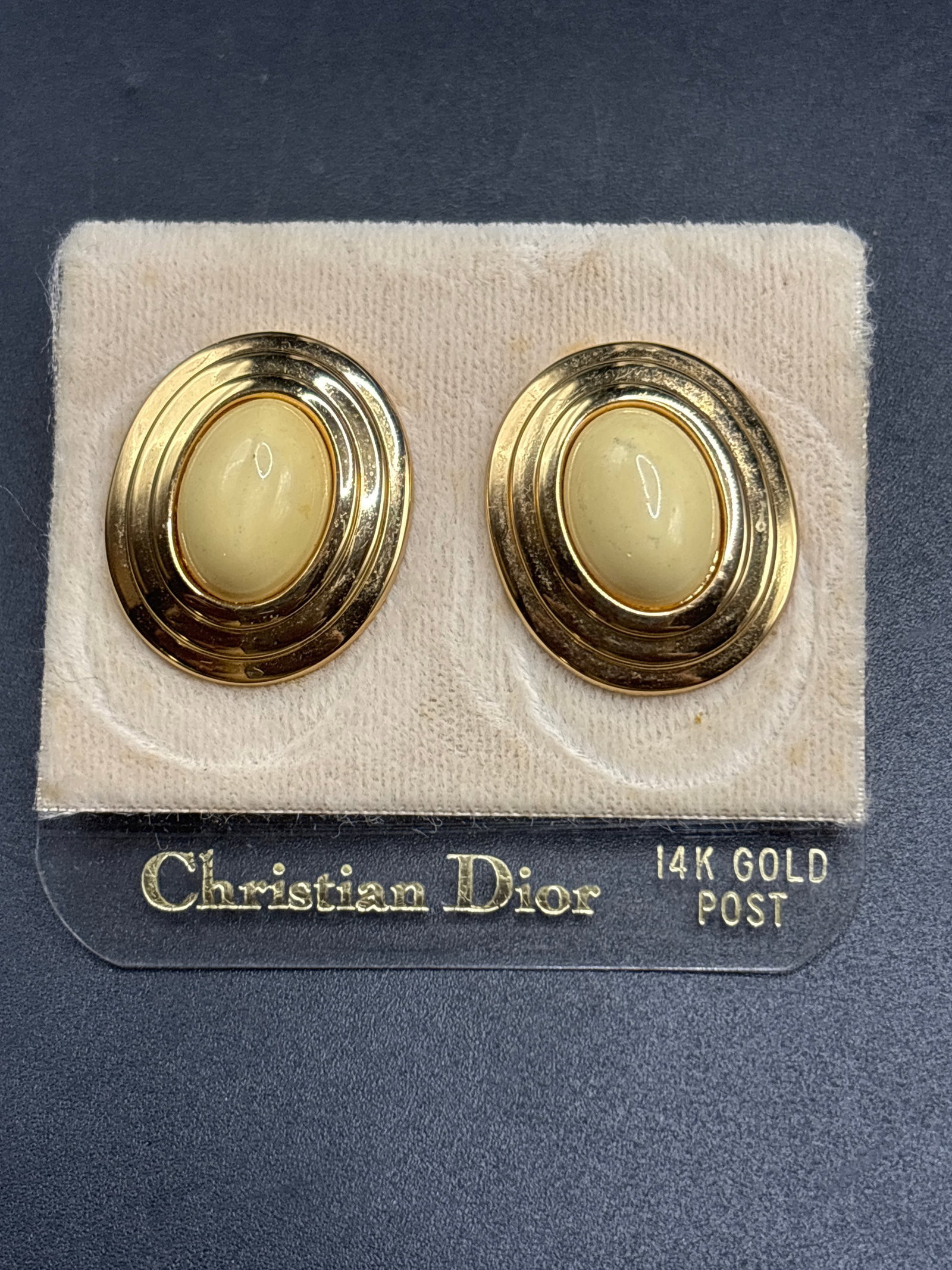 14K Gold Post vintage Christian Dior oval stud earrings: vintage Christian Dior oval stud earrings featuring smooth, creamy ivory/lucite cabochons framed by a polished gold-plated tiered border.They are presented on their original retail display card, which
