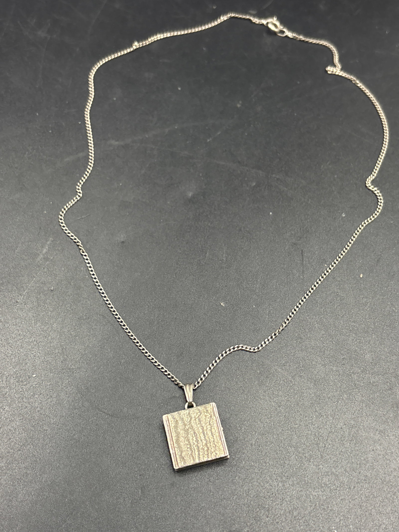 Sterling book form locket/pendant necklace: Sterling book form locket/pendant necklace featuring a textured front face suspended on a classic curb chain