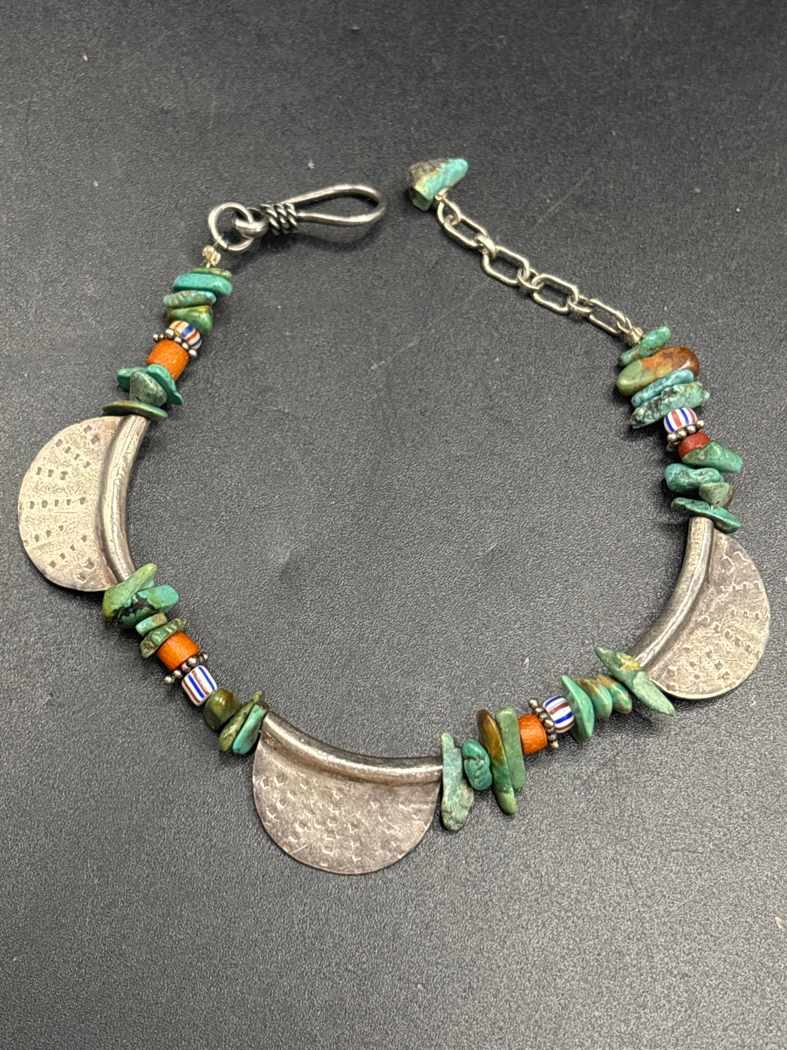 Sterling handmade beaded bracelet featuring turquoise stone: Sterling handmade beaded bracelet featuring turquoise stone chips, small orange-red spiny oyster or coral beads, striped trade beads, and three crescent-shaped textured silver components.