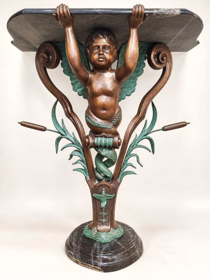 Continental Style Patinated Bronze Figural Putto Console Table with Marble: An elaborate figural console table featuring a winged putto supporting a shaped dark marble top, framed by scrolling supports and extensive classical and naturalistic ornament. The metalwork is finish