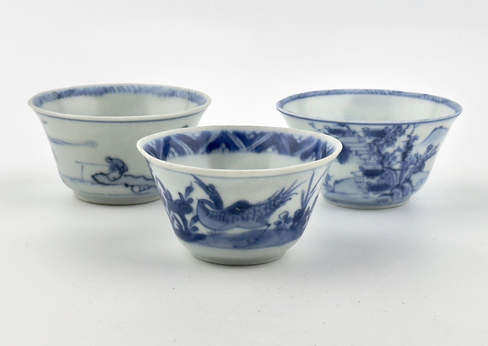 Three Chinoiserie Teabowl Set Circa 1725, Qing Dynasty, Yongzheng Reign: The left artwork is a classic blue-and-white porcelain teacup, adorned with a delicate landscape scene. The exterior of the cup features intricate details of trees, houses, mountains, and water, all d