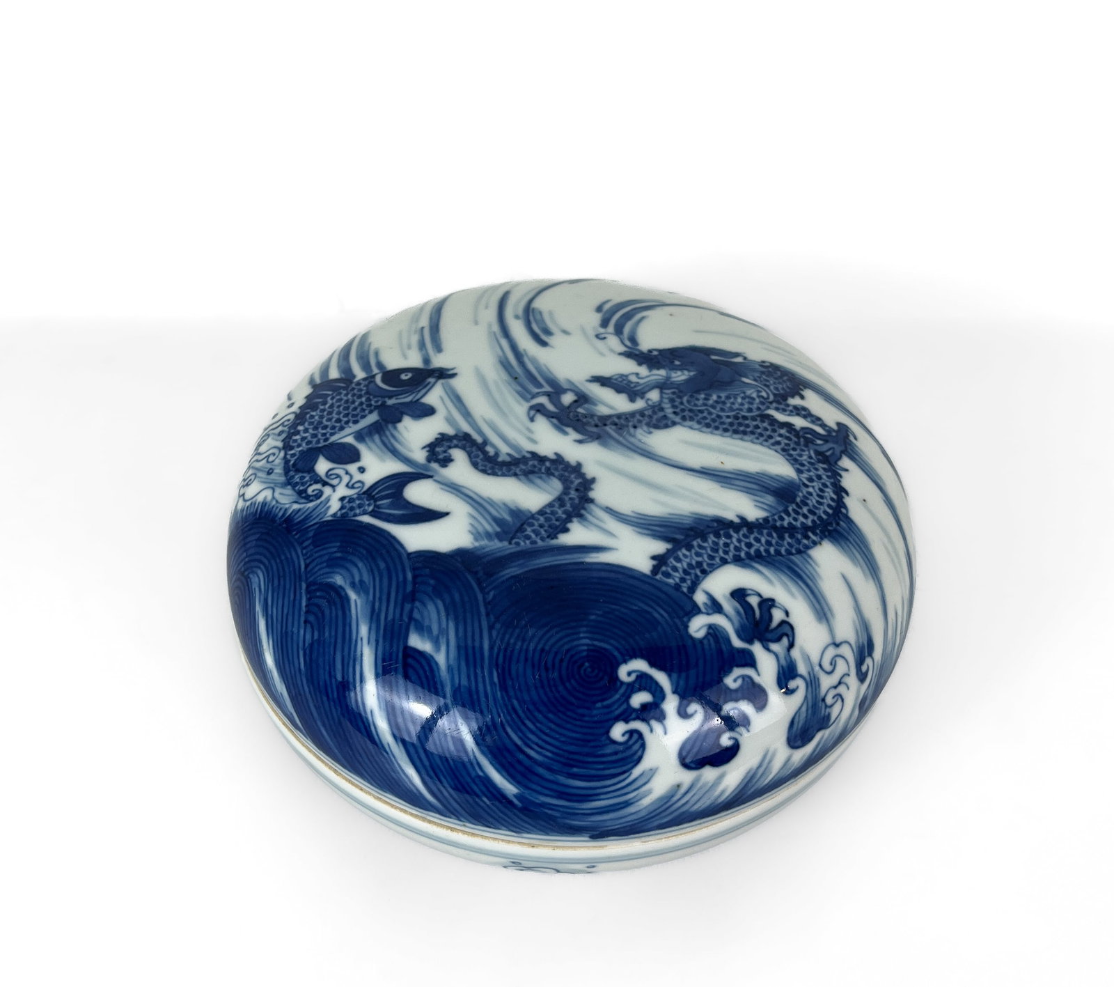 A CHINESE BLUE AND WHITE COVERED BOX WITH FISH AND DRAGON DECORATION, KANGXI PERIOD: A CHINESE BLUE AND WHITE COVERED BOX WITH FISH AND DRAGON DECORATION, KANGXI PERIOD 7.5 CM H. 16 CM DIAM. GOOD CONDITION