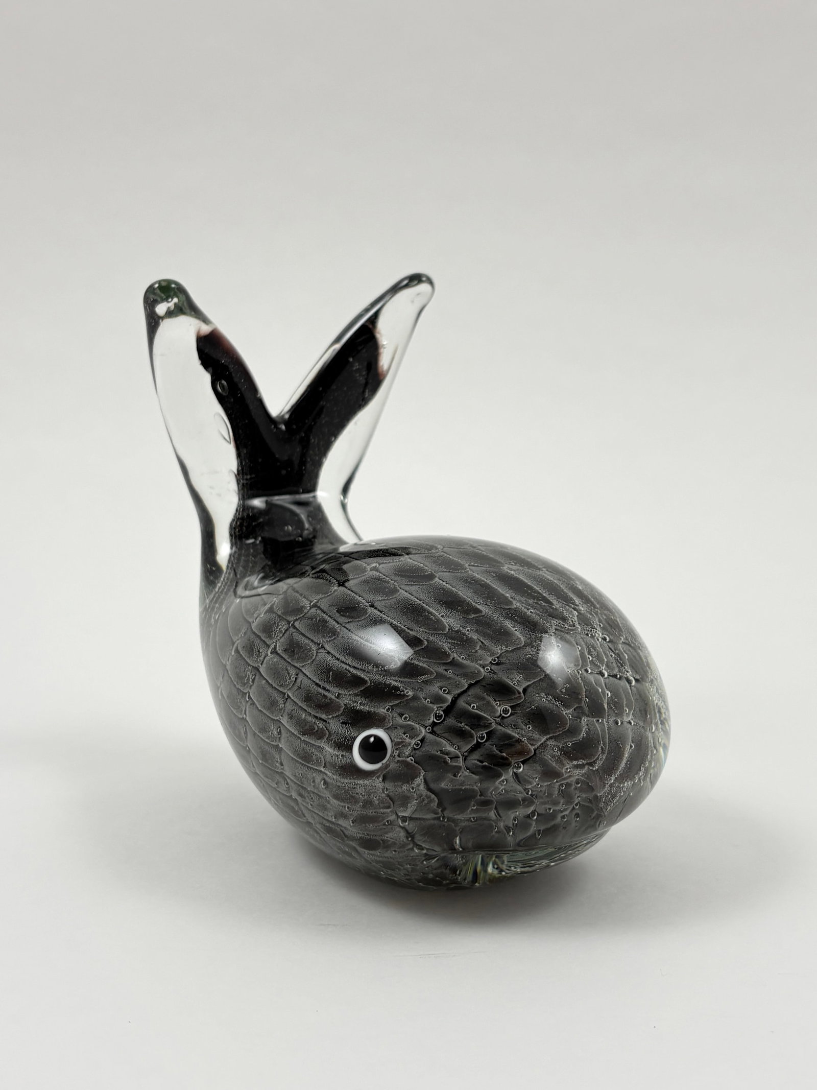 Murano Style Art Glass Whale Sculpture, 5 Inches Wide: Murano Art Glass Whale A charming Murano-style glass sculpture depicting a stylized whale with a textured, bubbled surface and wide tail fin. Crafted in deep charcoal-black glass with clear accents an