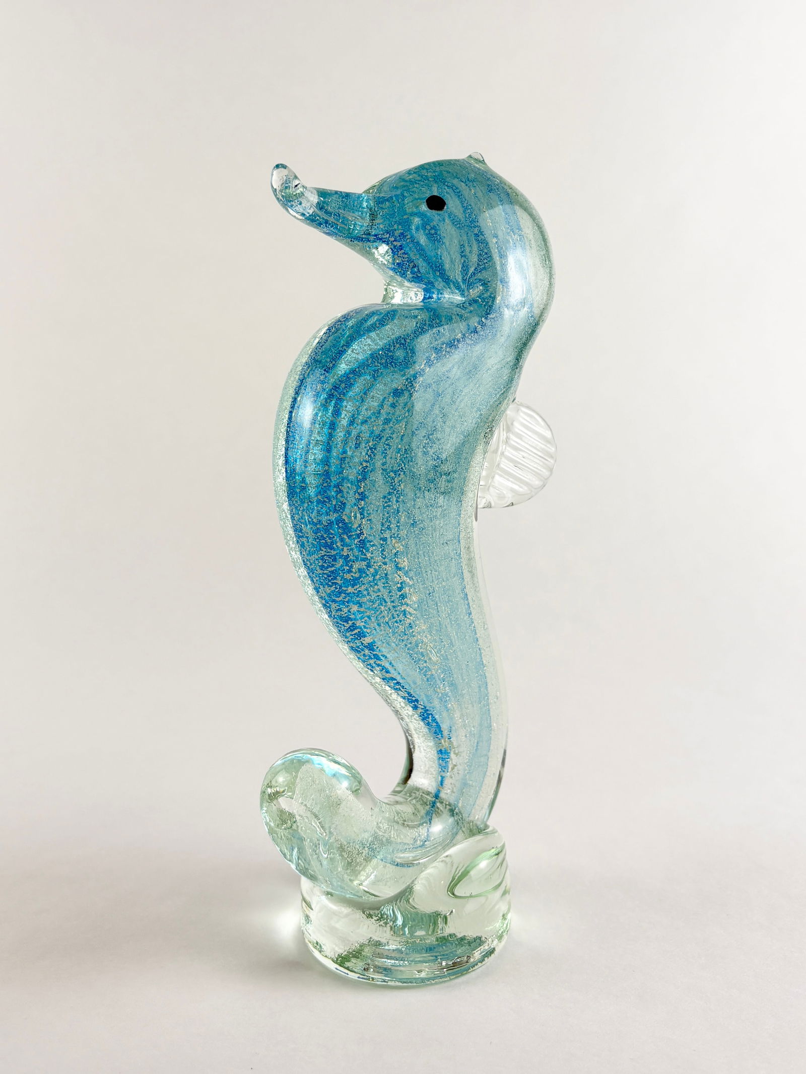 Murano-style Art Glass Seahorse: Art Glass Seahorse, Glass Seahorse Glass Height: 8 inches A decorative art glass seahorse in the style of Murano, featuring a blue-toned body with clear applied details and a sculpted base
