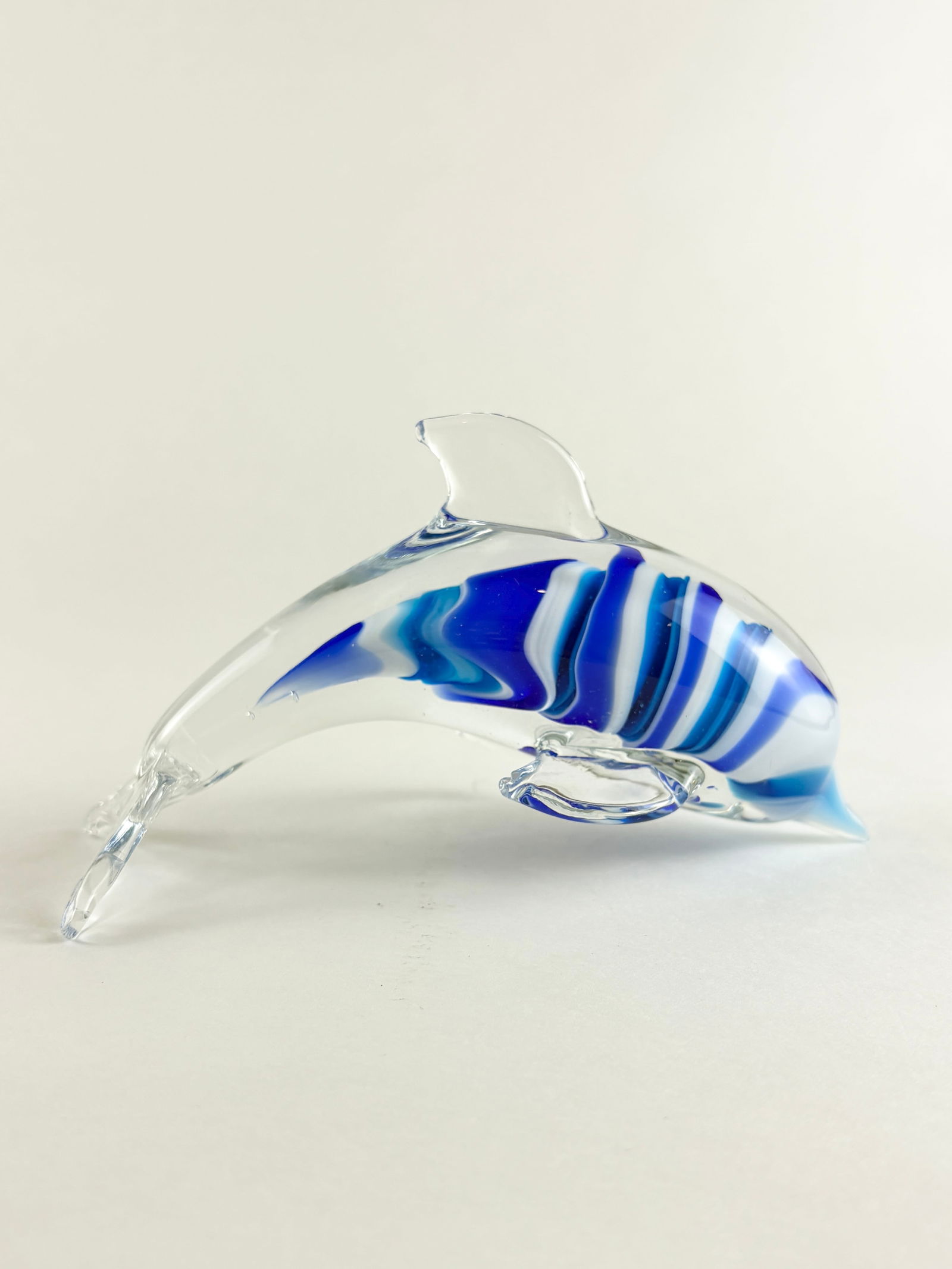 Art Glass Dolphin Sculpture: Art Glass Dolphin, Glass Dolphin Sculpture Glass Height: 6 inches Decorative art glass dolphin sculpture featuring a streamlined leaping form with layered blue and white internal striping encased in c