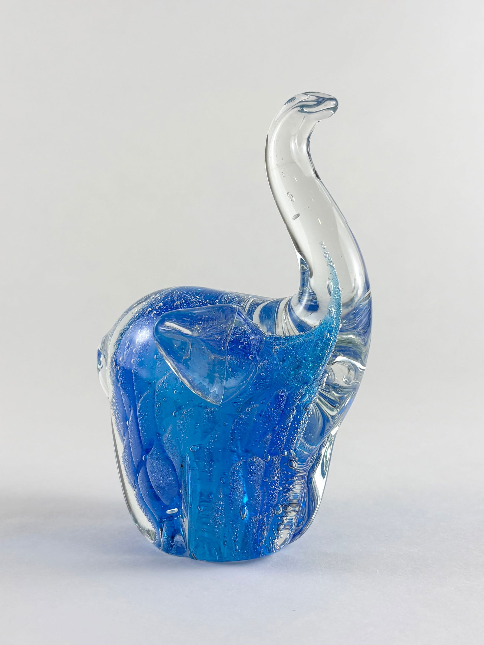 Glass Elephant Sculpture: Blue and clear art glass sculpture Handblown glass elephant rendered in deep cobalt blue with a clear applied trunk and layered glass detailing throughout the body. The form features subtle textural