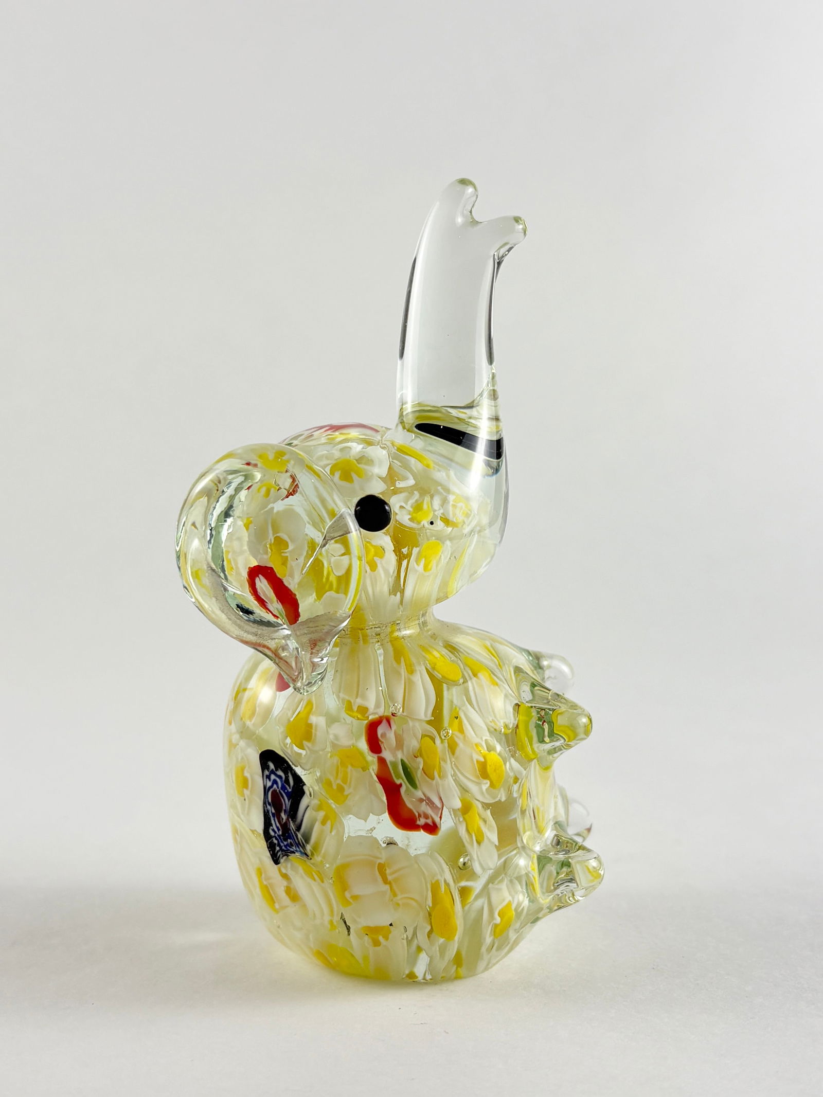 Glass Elephant Sculpture: Decorative hand-blown glass elephant sculpture with raised trunk and stylized body form. Executed in clear glass with dense yellow coloration and multicolored inclusions dispersed throughout, includin