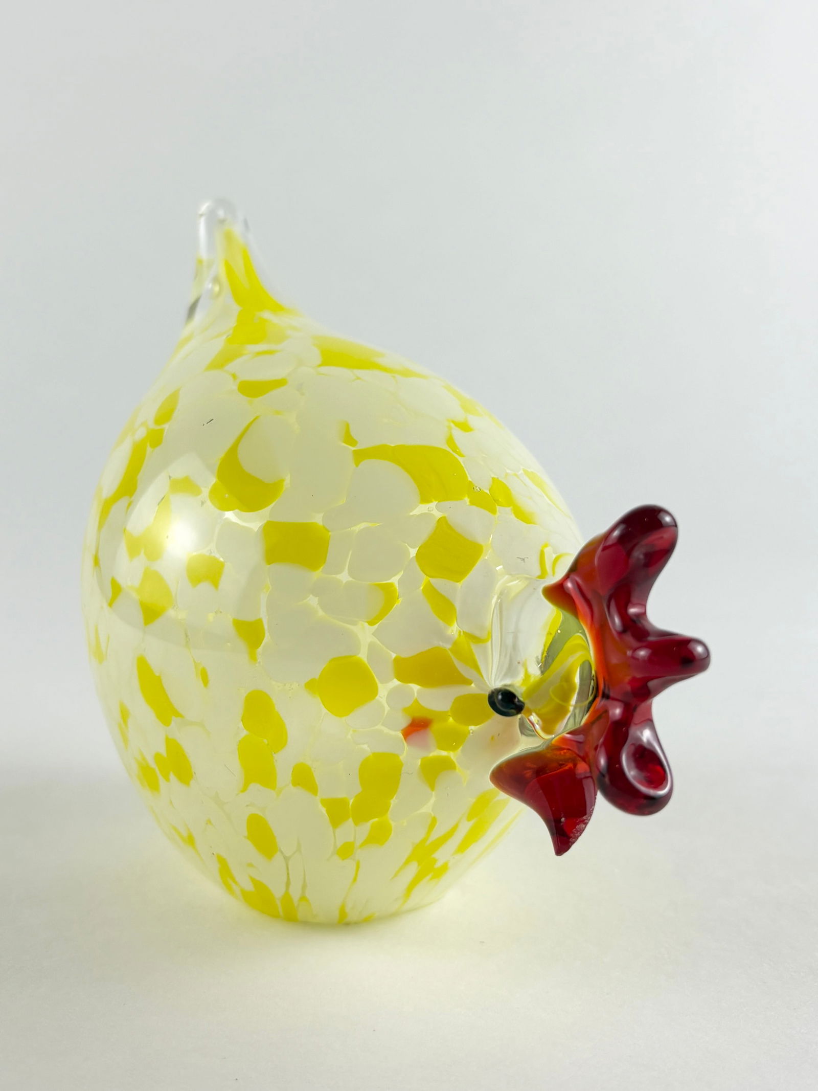 Glass Hen Sculpture: Decorative hand-blown glass hen sculpture featuring a yellow speckled body with applied red glass comb and beak details. Compact sculptural form intended for tabletop or shelf display. Height: 5