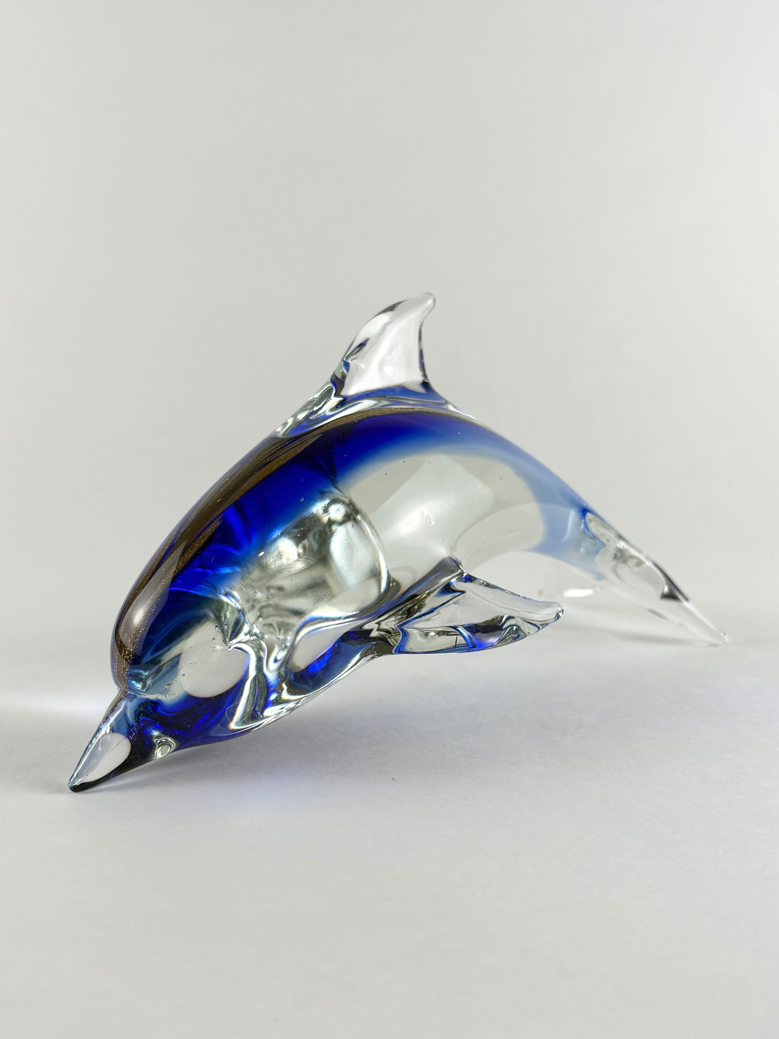 Glass Dolphin Sculpture: Hand-blown glass dolphin sculpture in a leaping pose, executed in clear glass with deep cobalt blue accents along the back and fins. The streamlined form and fluid contours emphasize motion, making