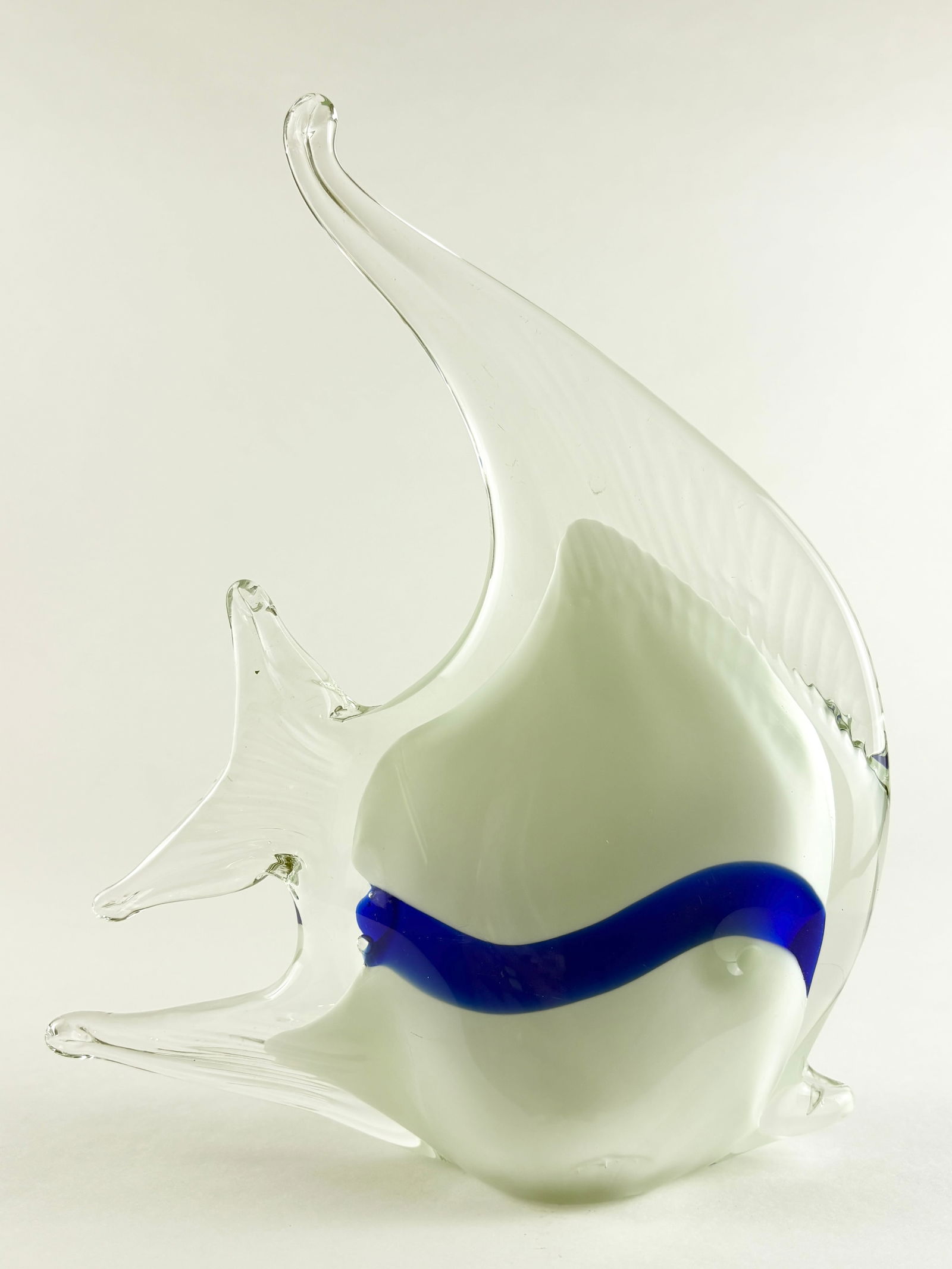 Glass Fish Sculpture: Hand-blown glass fish sculpture featuring an opaque white body accented by a bold cobalt-blue band and clear, flowing fins. The elongated dorsal fin and sculpted tail create a sense of motion, while t