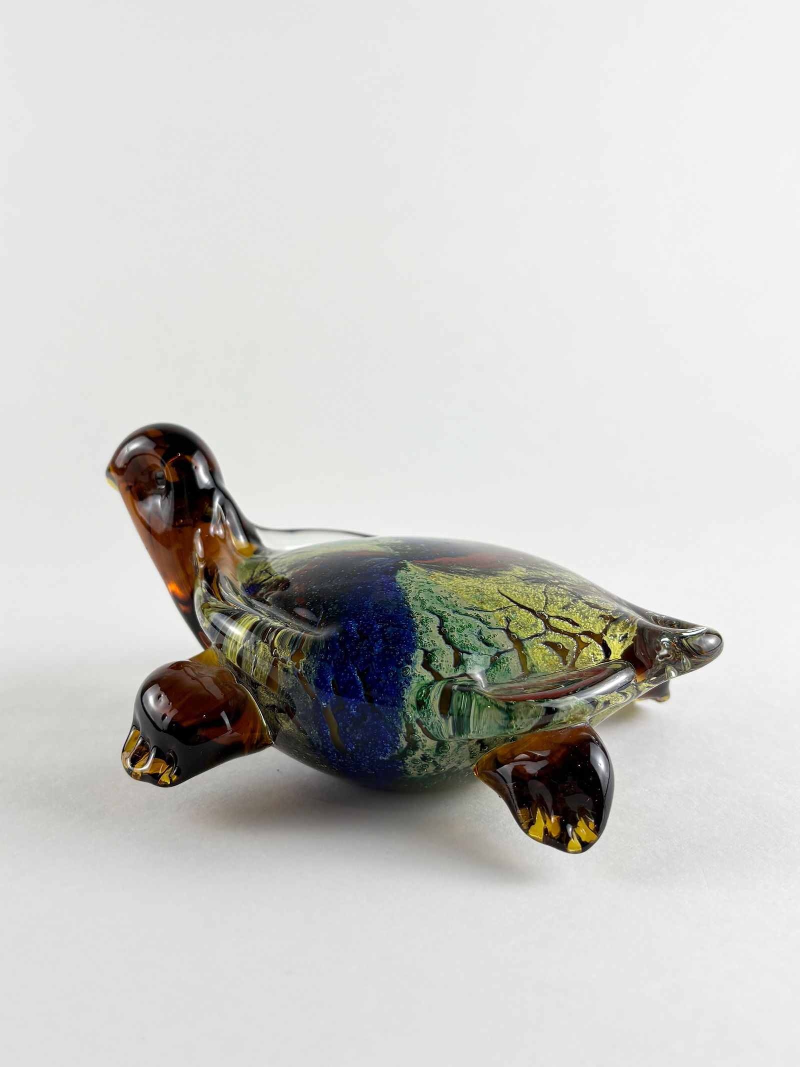 Glass Turtle Sculpture: Hand-blown glass turtle sculpture featuring a rounded shell form with mottled blue, green, and amber tones. The piece is executed in solid art glass with applied legs and head, displaying swirling int