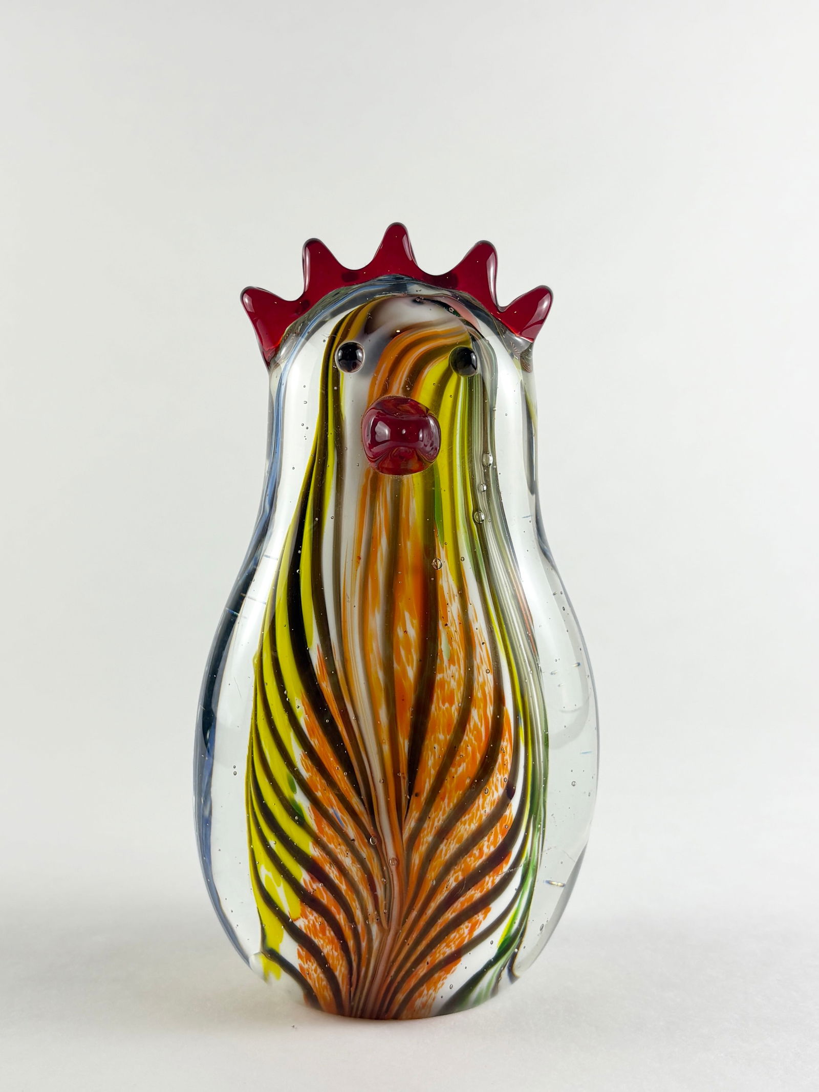 Glass Chicken Sculpture: Hand-blown glass chicken sculpture featuring a vertically striped body in amber, yellow, green, and blue tones, finished with a red comb and beak. The form displays controlled internal striping and
