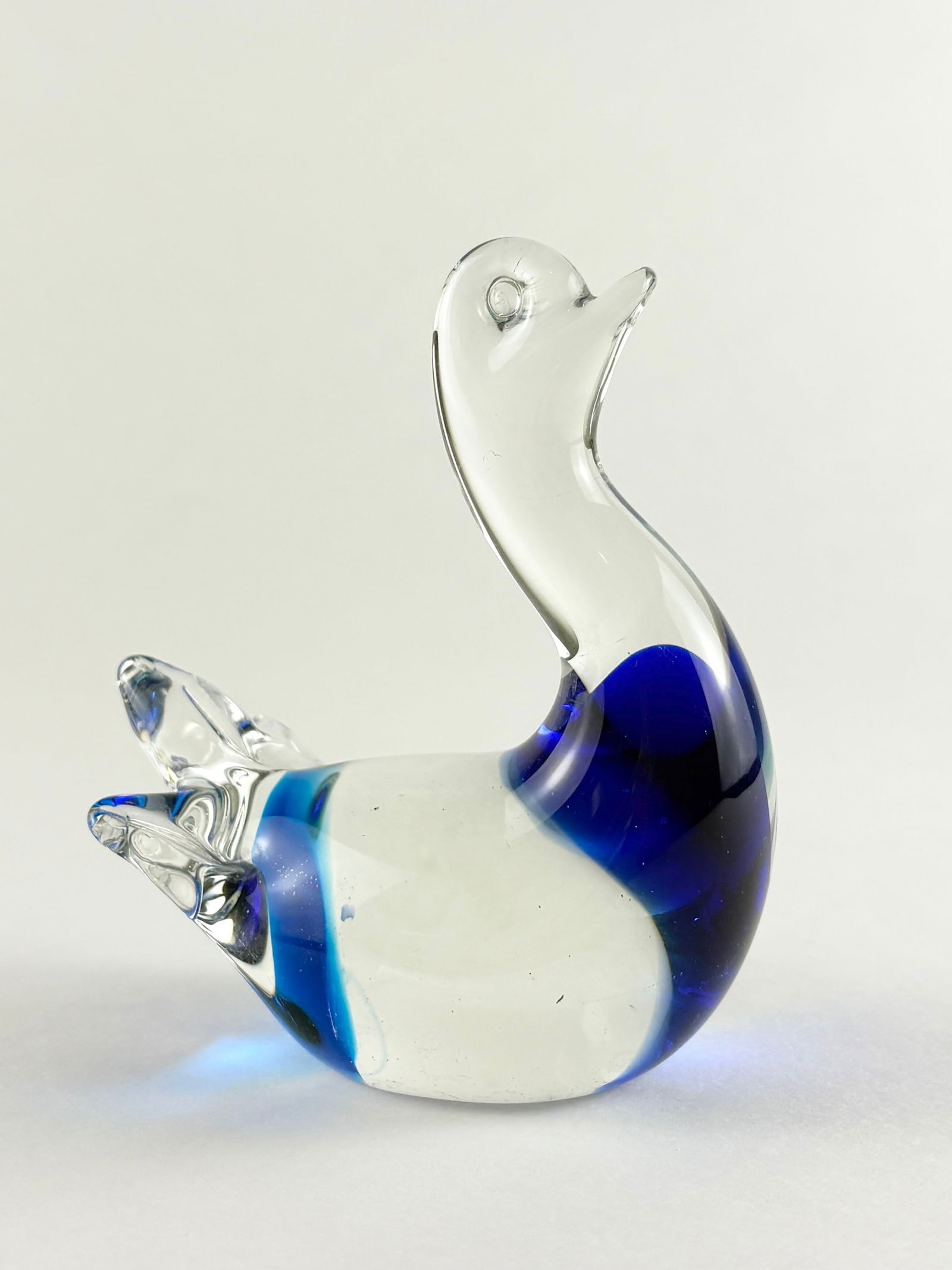 Glass Swan Sculpture: Clear and cobalt-blue art glass swan sculpture with an elongated, curved neck and stylized body form. The piece features layered transparent and blue glass with a smooth, polished finish, giving it a