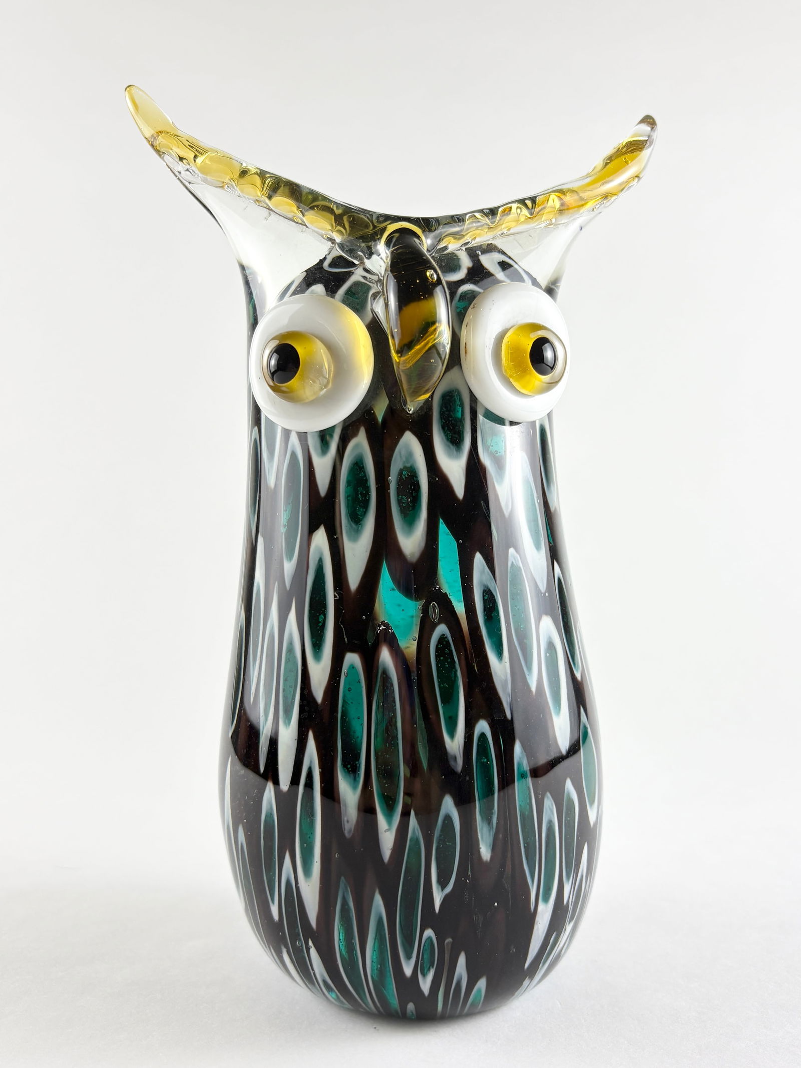 Glass Owl Sculpture: Hand-blown glass owl sculpture featuring a tall stylized form with applied eyes and extended ear tufts. Executed in layered black, teal, and clear glass with mottled surface decoration and yellow