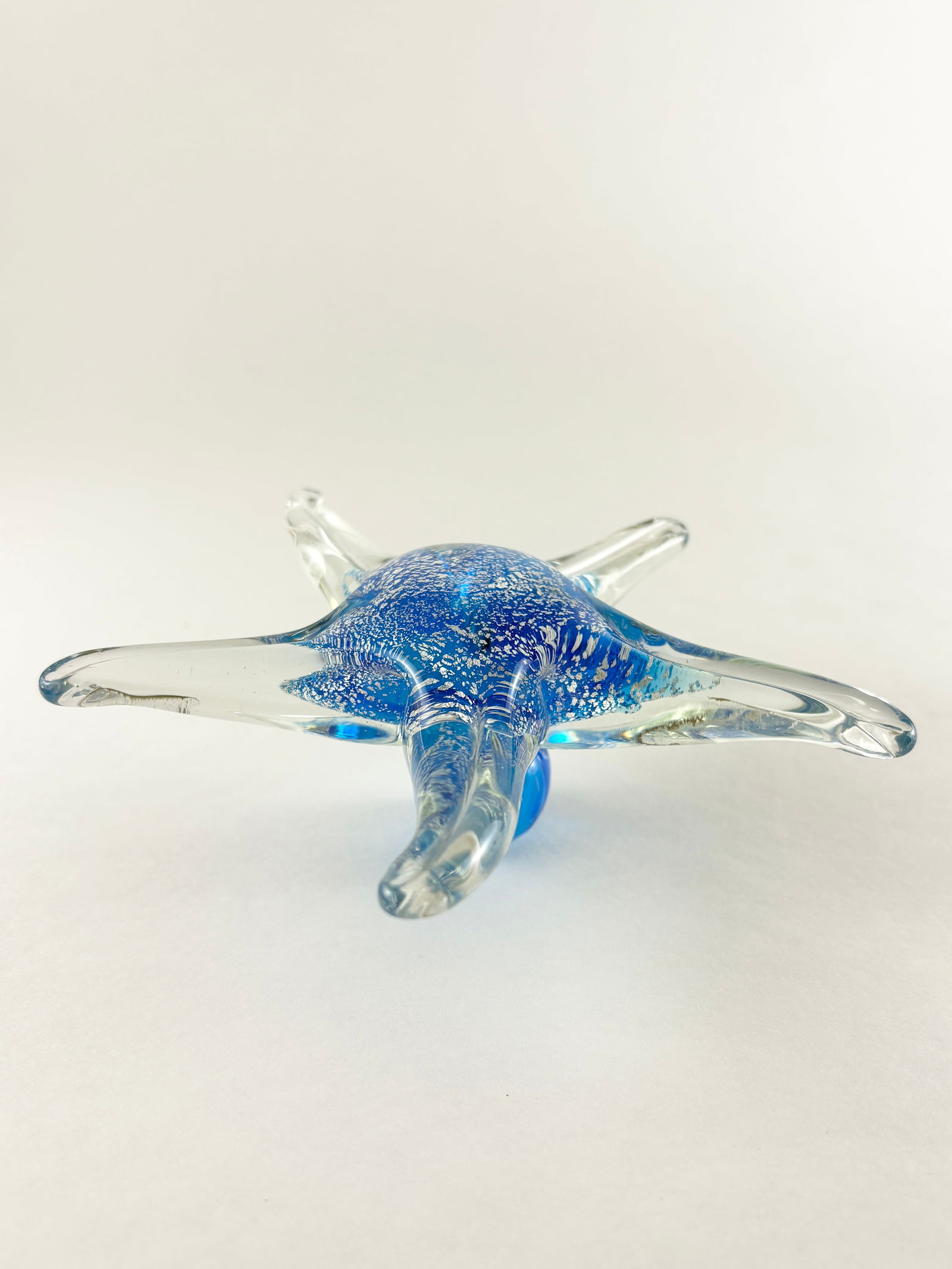 Murano Style Glass Starfish Sculpture: Murano style hand-blown glass starfish sculpture with a low-profile, symmetrical form. Executed in clear glass with a vibrant blue core featuring controlled bubble and particulate effects, extending