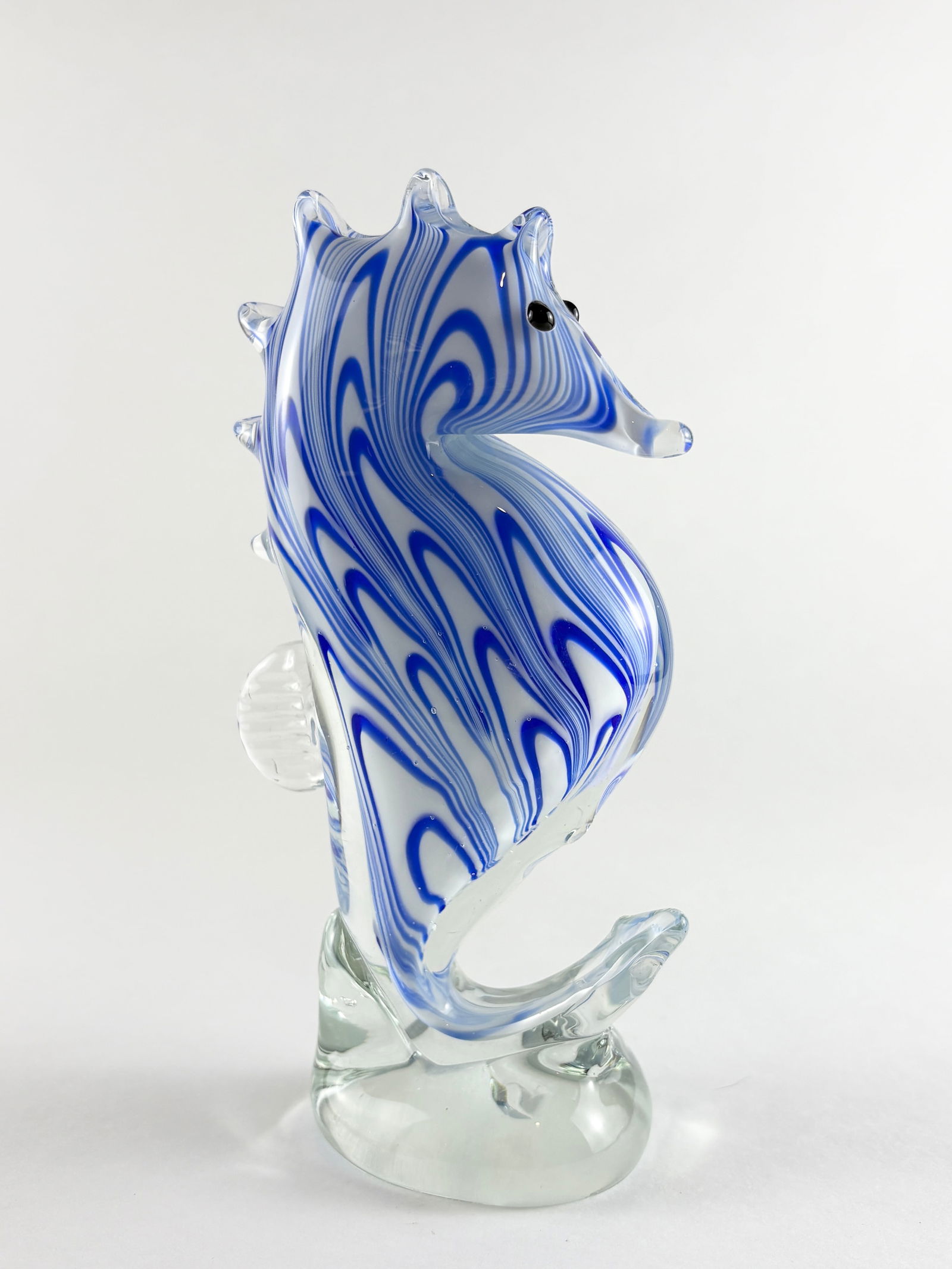Murano Style Glass Seahorse Sculpture: Murano style hand-blown glass seahorse sculpture featuring cobalt blue and white swirling cane decoration, executed in an upright form with applied fins and curled tail mounted on a clear glass base.
