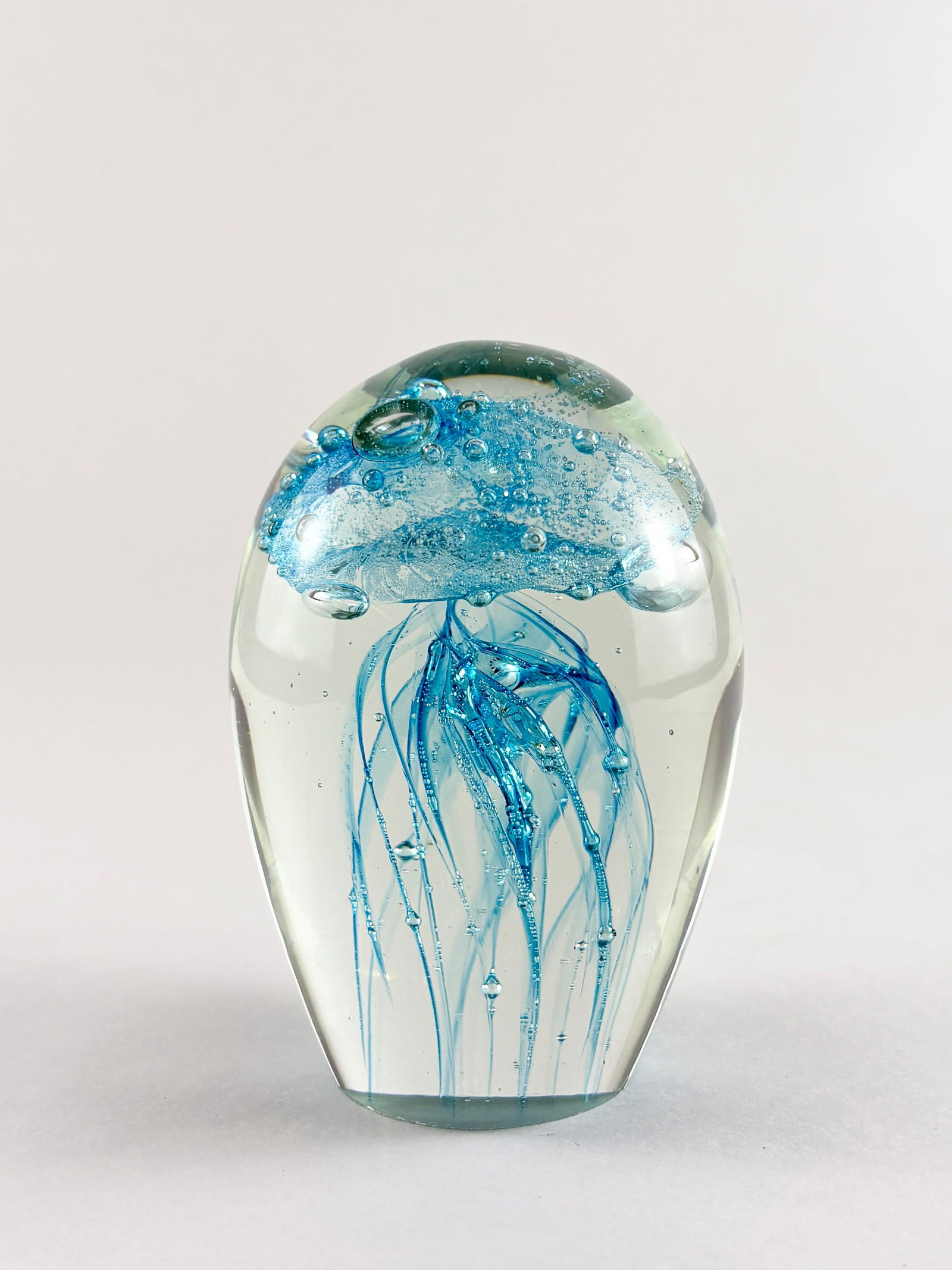 Art Glass Jellyfish Sculpture: Decorative art glass jellyfish sculpture featuring a clear rounded form with suspended blue glass tendrils and internal detailing, creating a floating, underwater visual effect. Executed in a