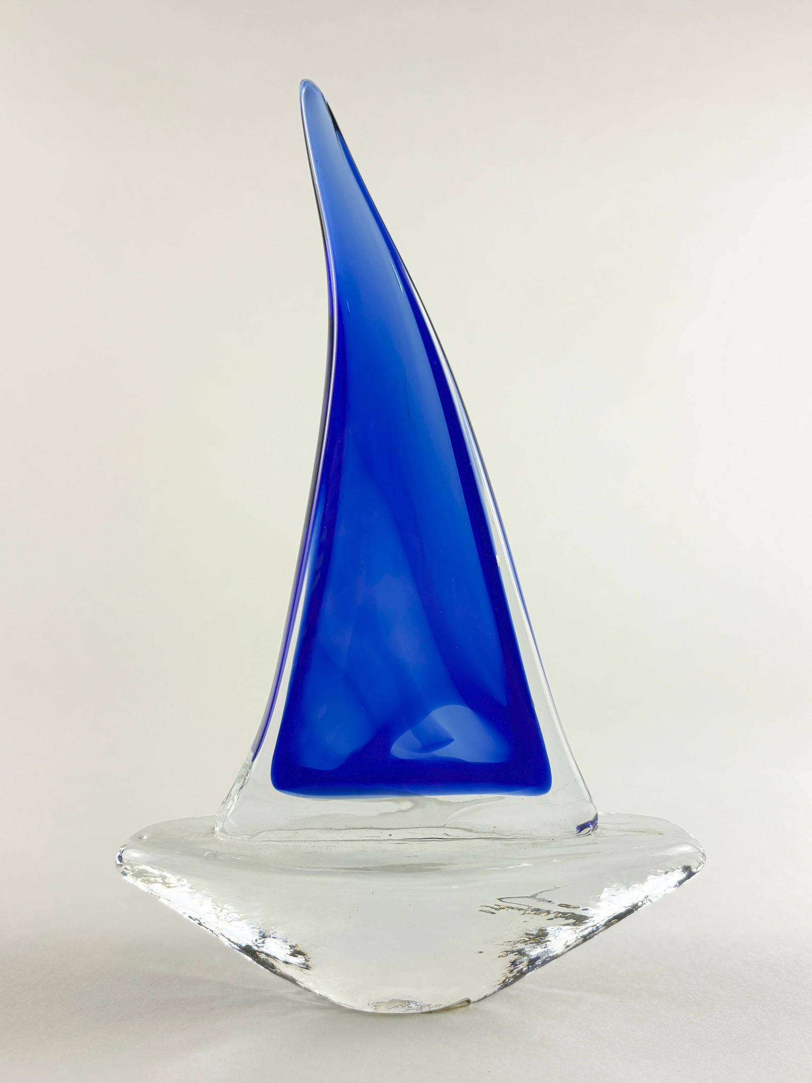 Murano Style Art Glass Sailboat Sculpture: Decorative art glass sailboat sculpture in the Murano style, featuring a tall cobalt blue sail rising from a clear glass hull with fluid, hand-formed contours. The minimalist nautical form emphasizes