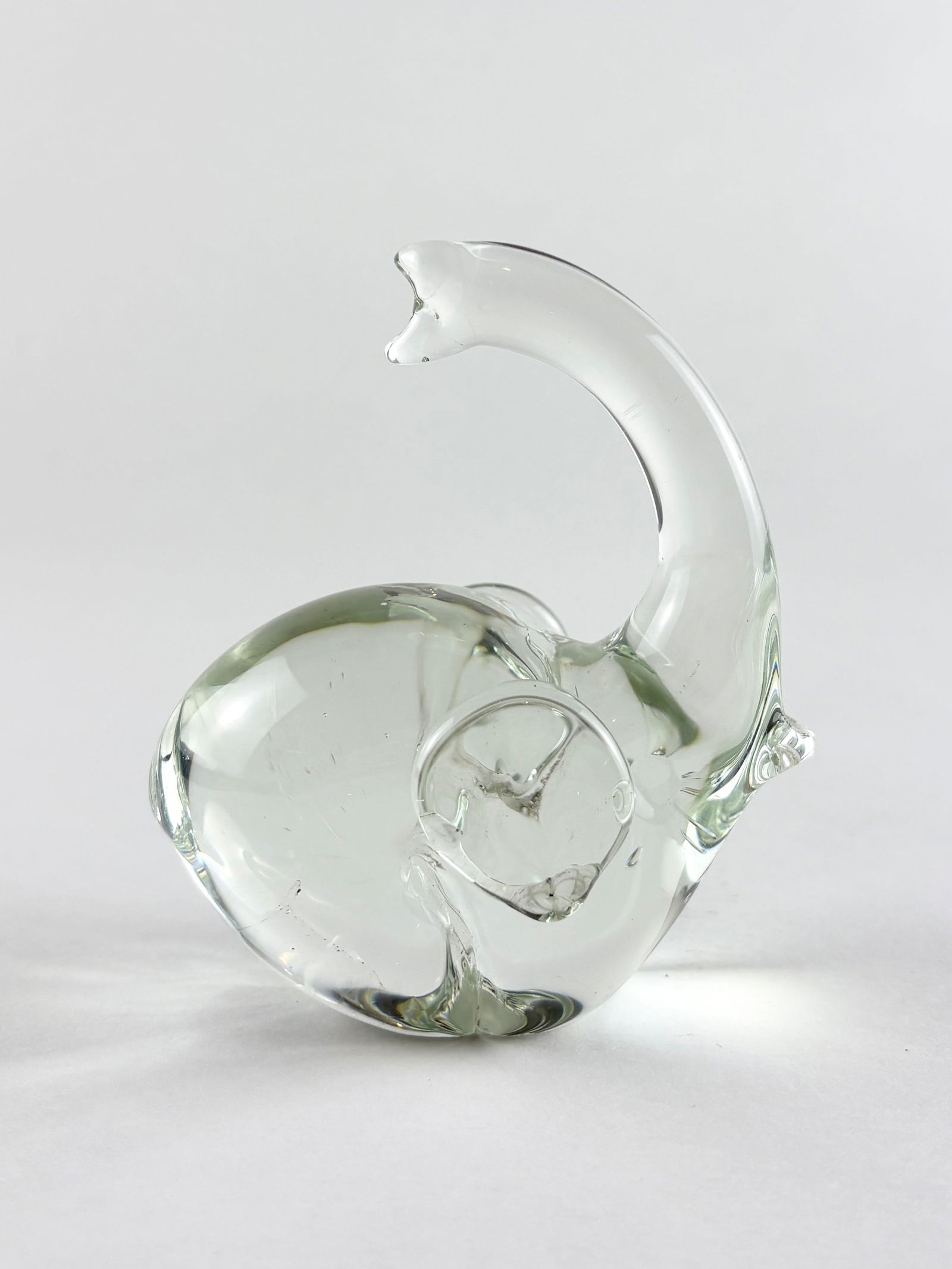 Art Glass Elephant Sculpture: Decorative clear art glass elephant sculpture featuring a rounded body with an upturned trunk and applied spiral detail along the flank. The minimalist, hand-formed design emphasizes transparency and