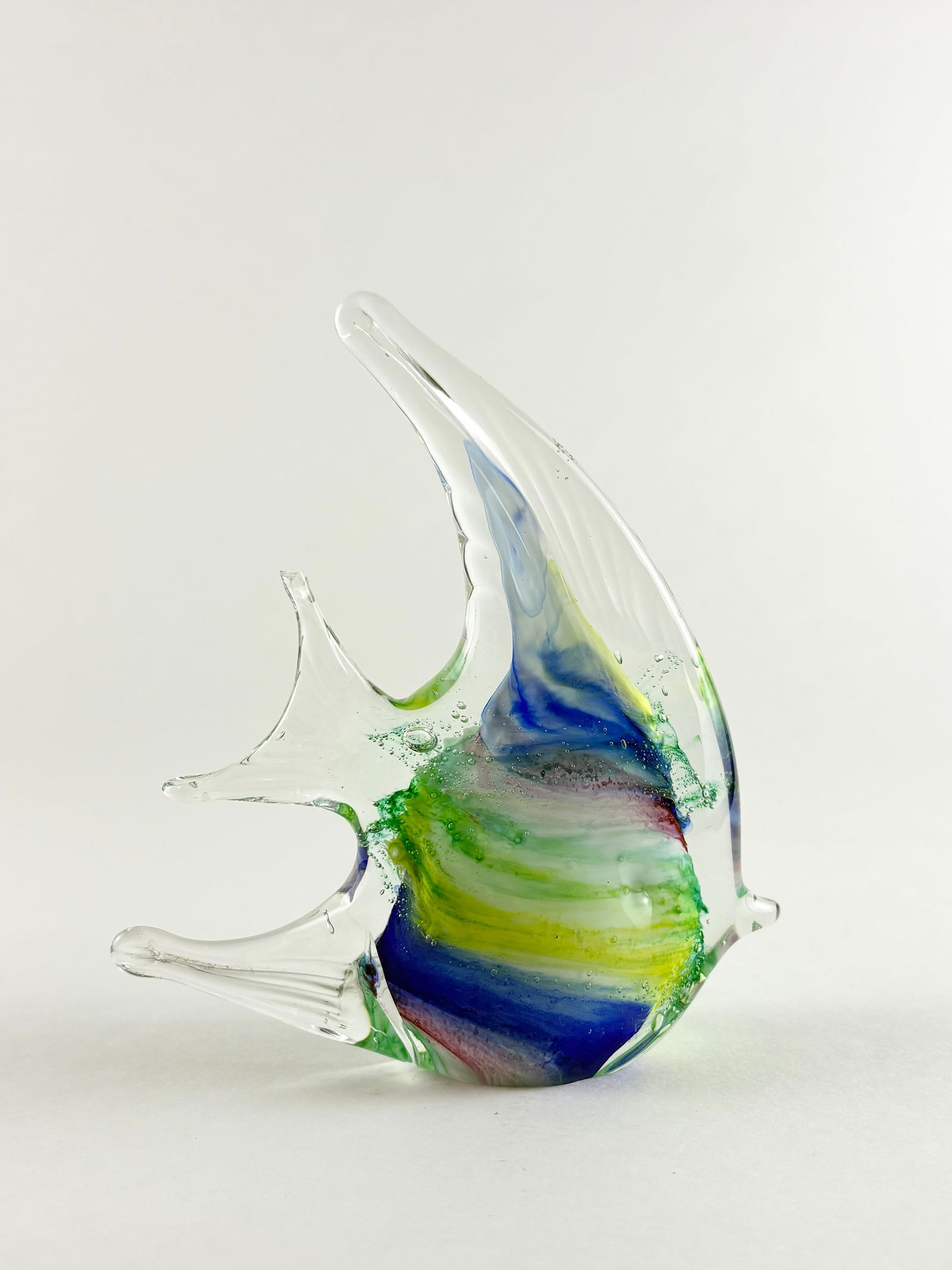Murano-Style Art Glass Fish Sculpture: Decorative hand-blown art glass fish sculpture featuring layered blue, green, and yellow coloration with clear fins and an elongated dorsal form. The flowing internal color bands and sculptural silhou