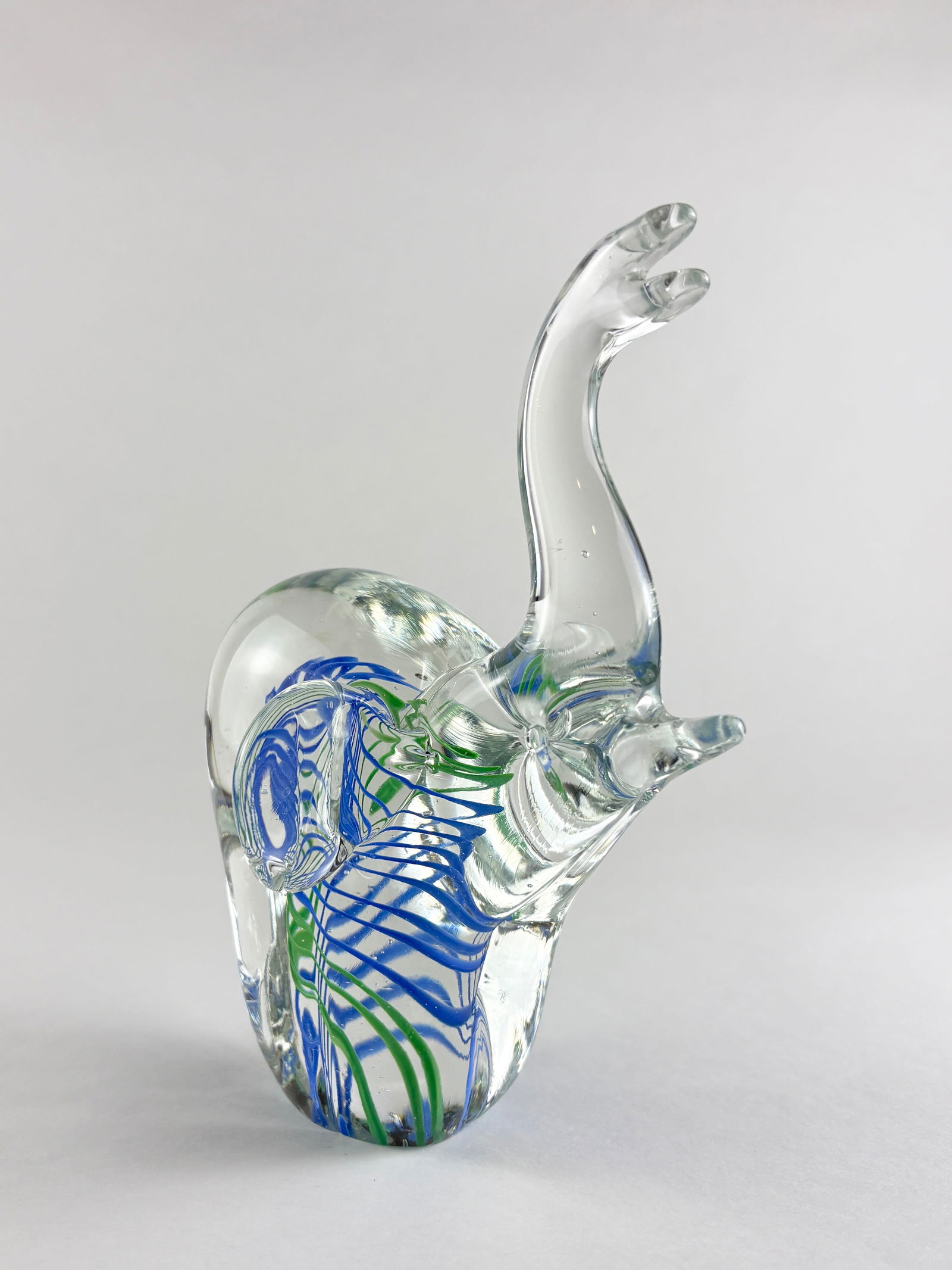 Glass Elephant Sculpture (Murano Style): Decorative art glass elephant sculpture featuring a clear blown body with applied blue and green trailing decoration throughout the form. The figure is modeled with an elongated raised trunk, rounded
