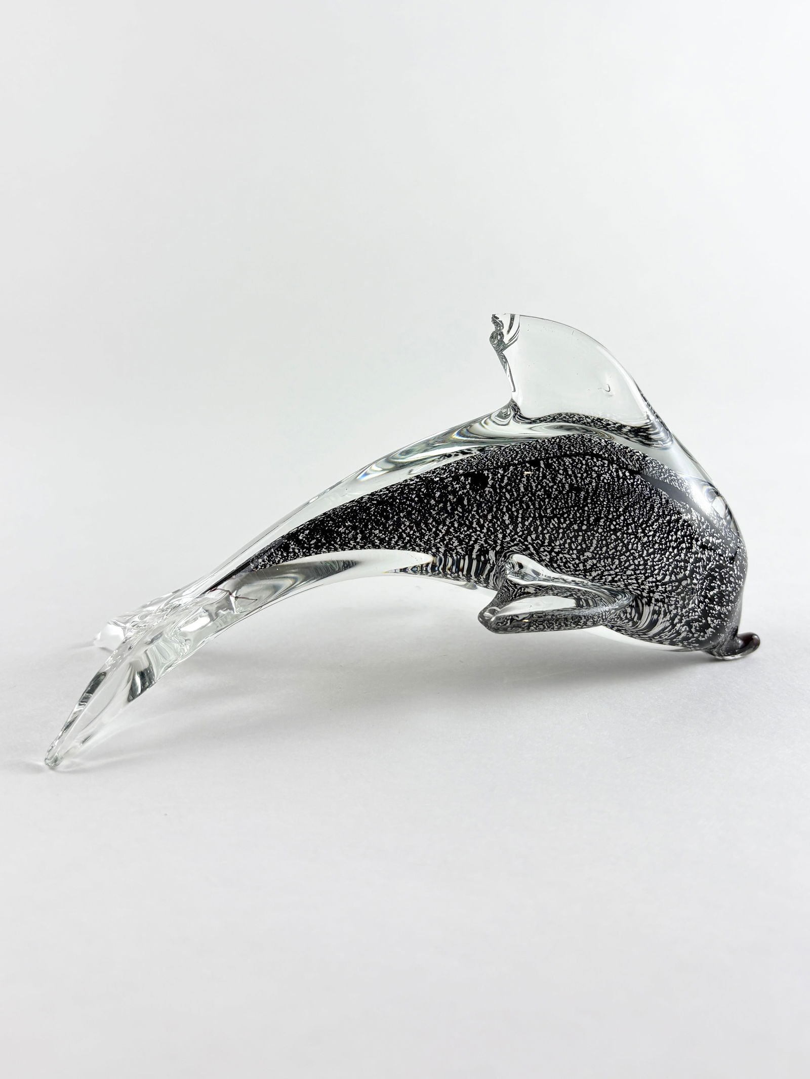 Glass Dolphin Sculpture (Murano Style): Decorative art glass dolphin sculpture rendered in clear and dark gray glass with an elongated, streamlined form. The piece features a speckled interior core encased in clear glass, with applied fins